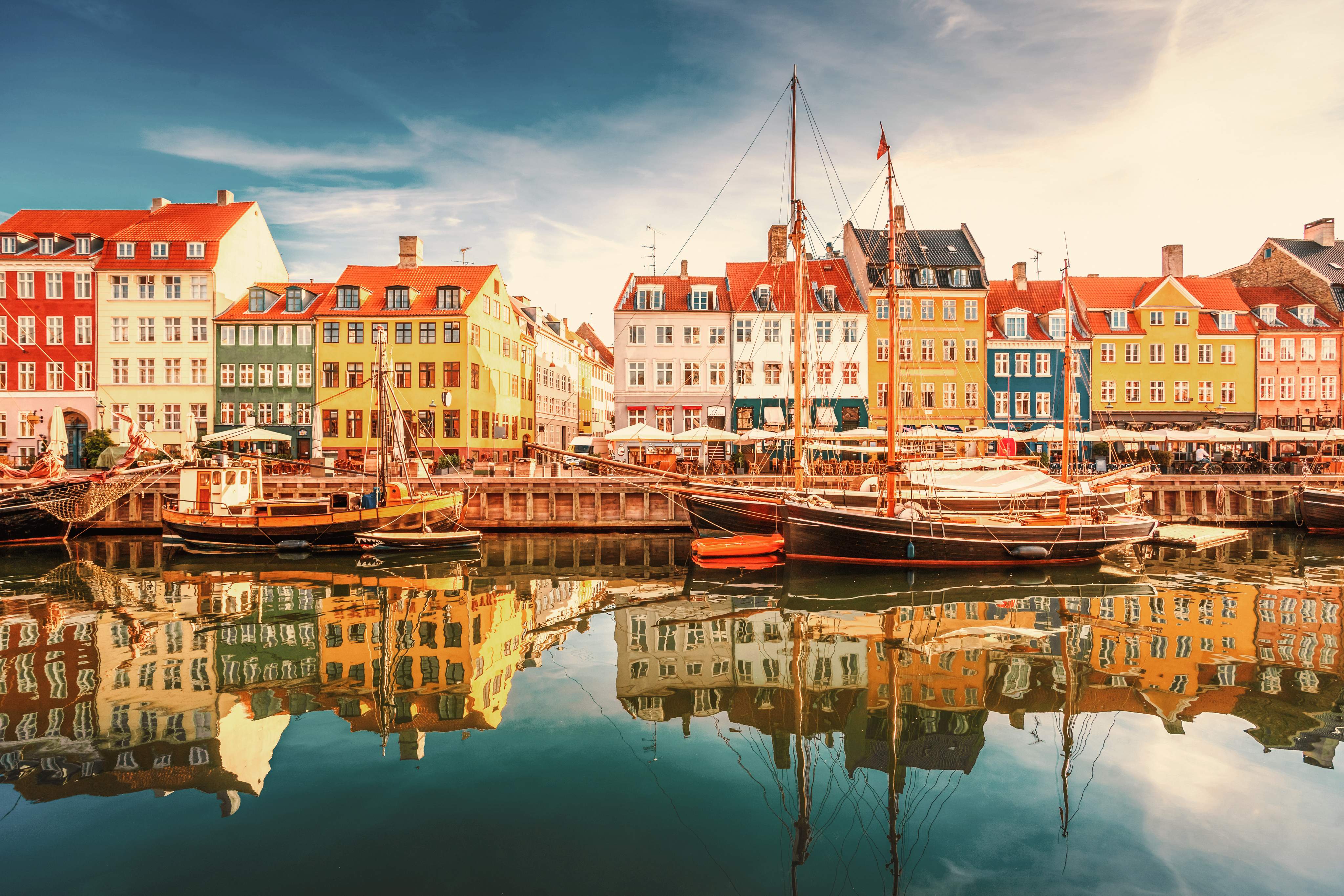 Colorful historic houses and sailing boats at Nyhavn harbor in Copenhagen, Denmark, at sunset.