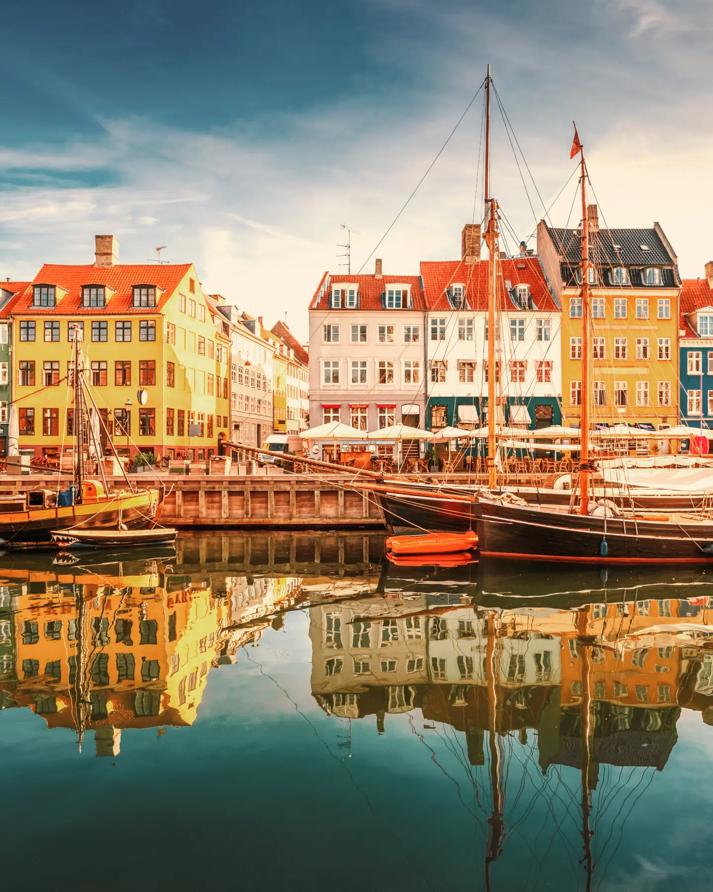 Colorful historic houses and sailing boats at Nyhavn harbor in Copenhagen, Denmark, at sunset.