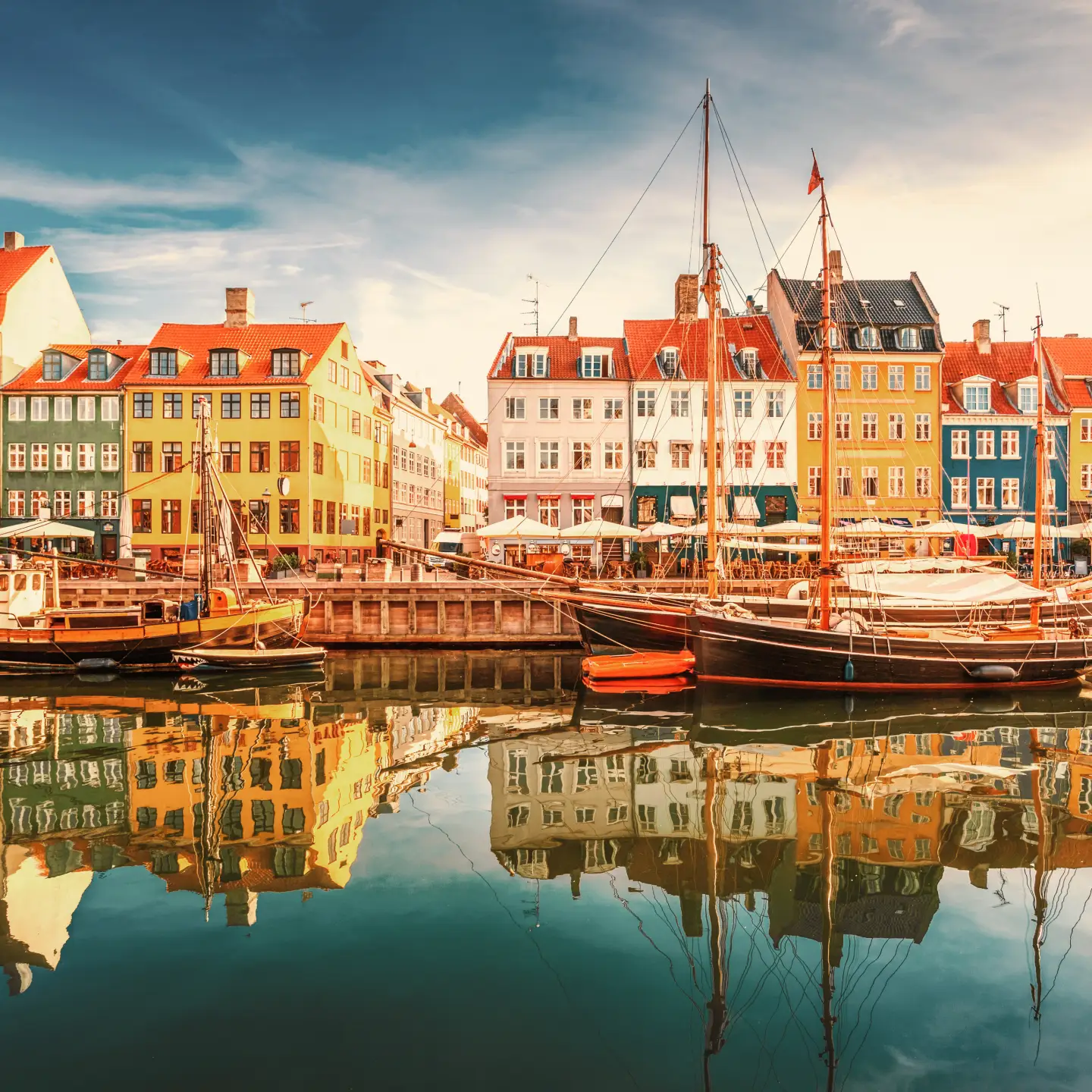 Colorful historic houses and sailing boats at Nyhavn harbor in Copenhagen, Denmark, at sunset.