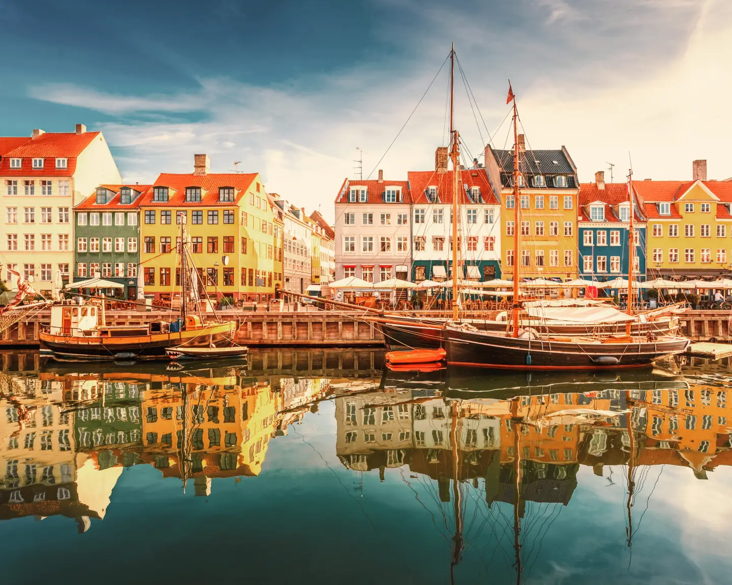 Colorful historic houses and sailboats at Nyhavn Harbor in Copenhagen, Denmark, at sunset.
