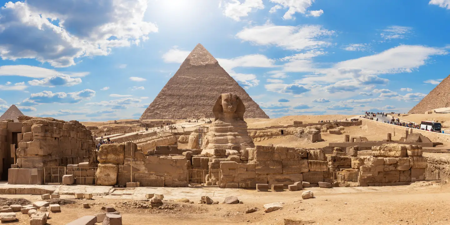 Blick auf die Große Sphinx und die Pyramiden von Gizeh bei Kairo unter blauem Himmel mit vereinzelten Wolken.