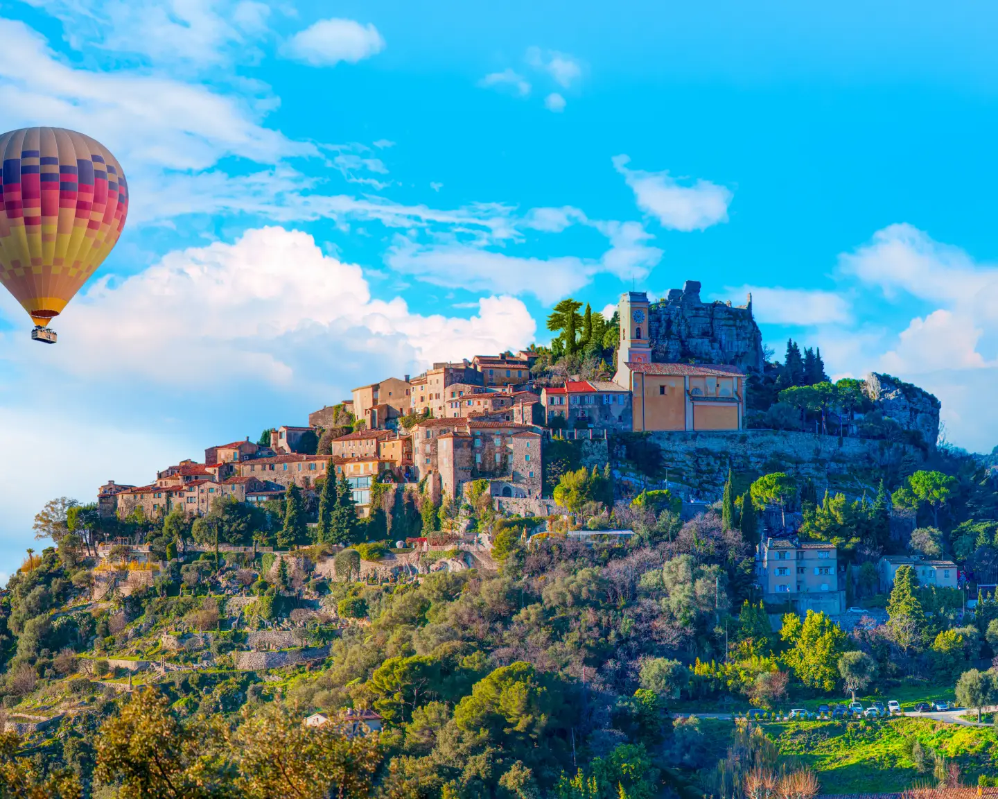 Blick auf das mittelalterliche Bergdorf Èze an der Côte d’Azur mit historischen Steinhäusern, mediterraner Landschaft und einem Heißluftballon am Himmel.