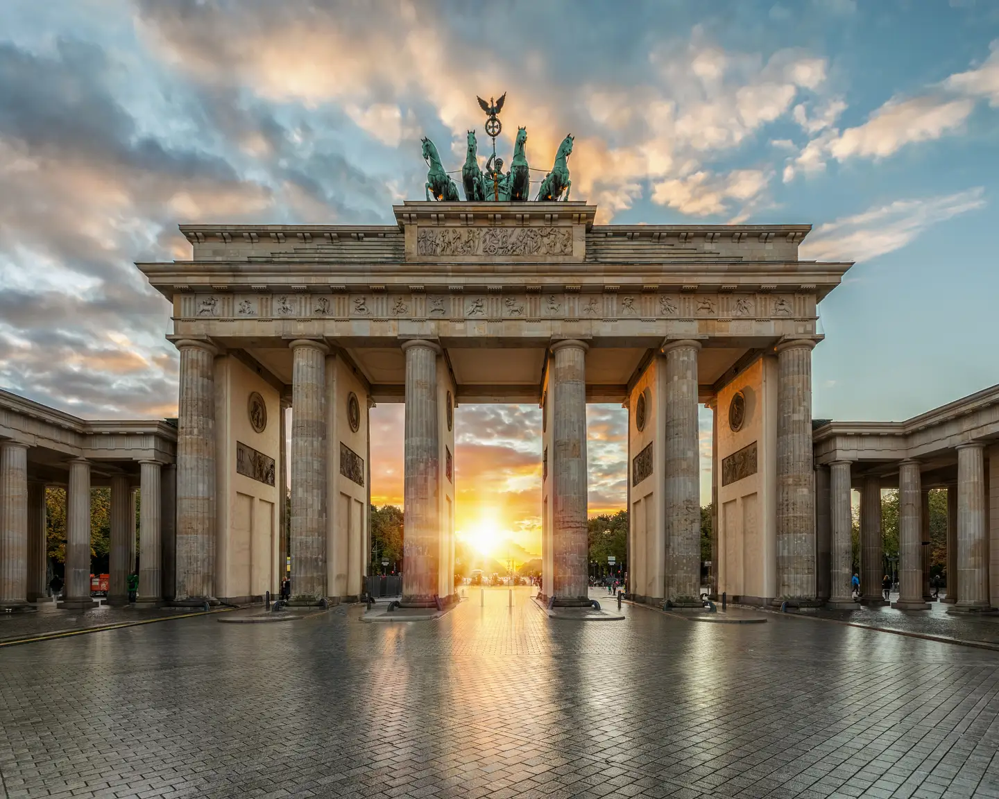 La puerta de Brandeburgo en Berlín al amanecer, con el sol brillando a través de las columnas e iluminando el cielo con tonos cálidos.