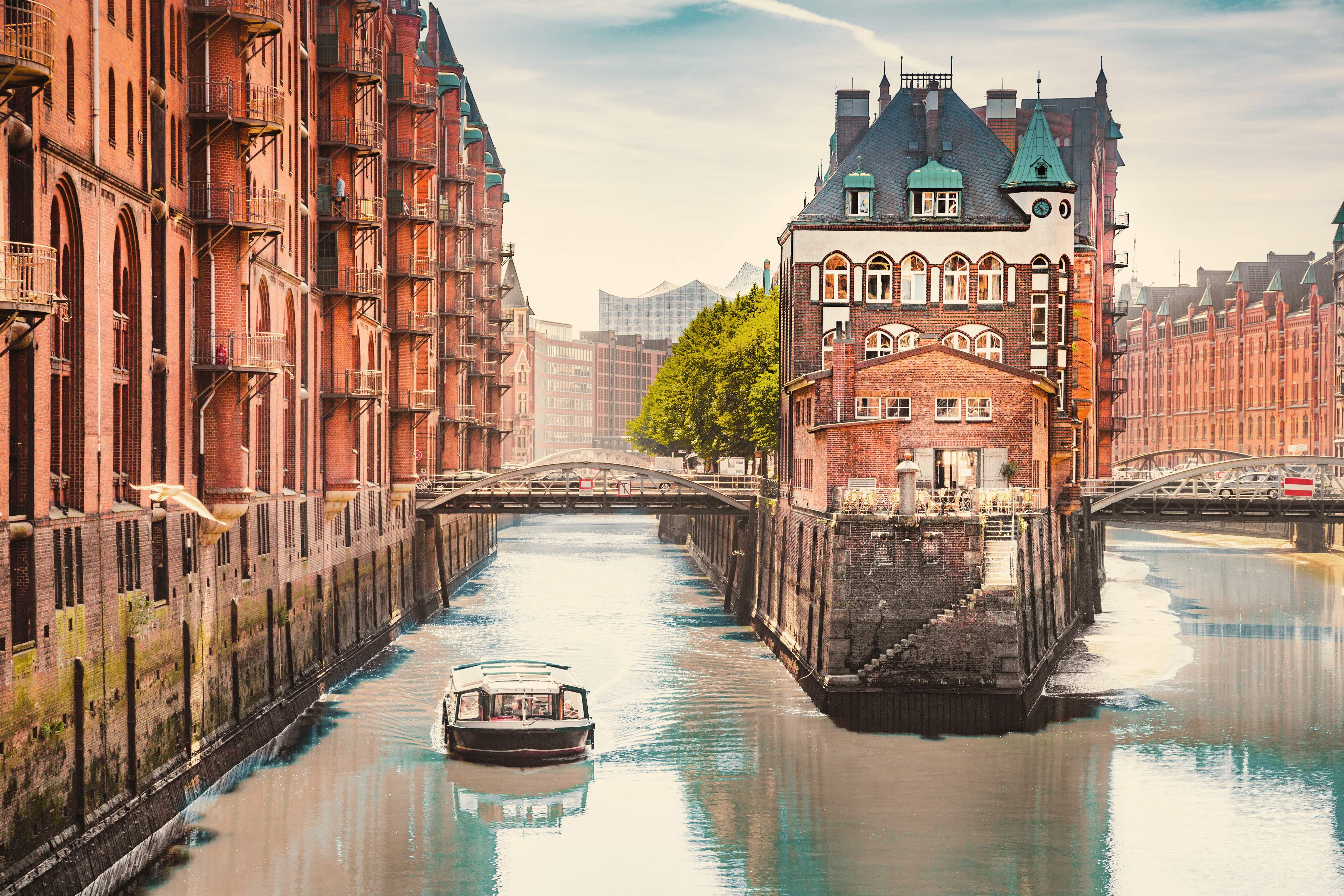 Wasserschloss in der Hamburger Speicherstadt mit Backsteinfassaden, Kanälen, Brücken und einem Ausflugsboot auf dem Wasser bei weichem Tageslicht