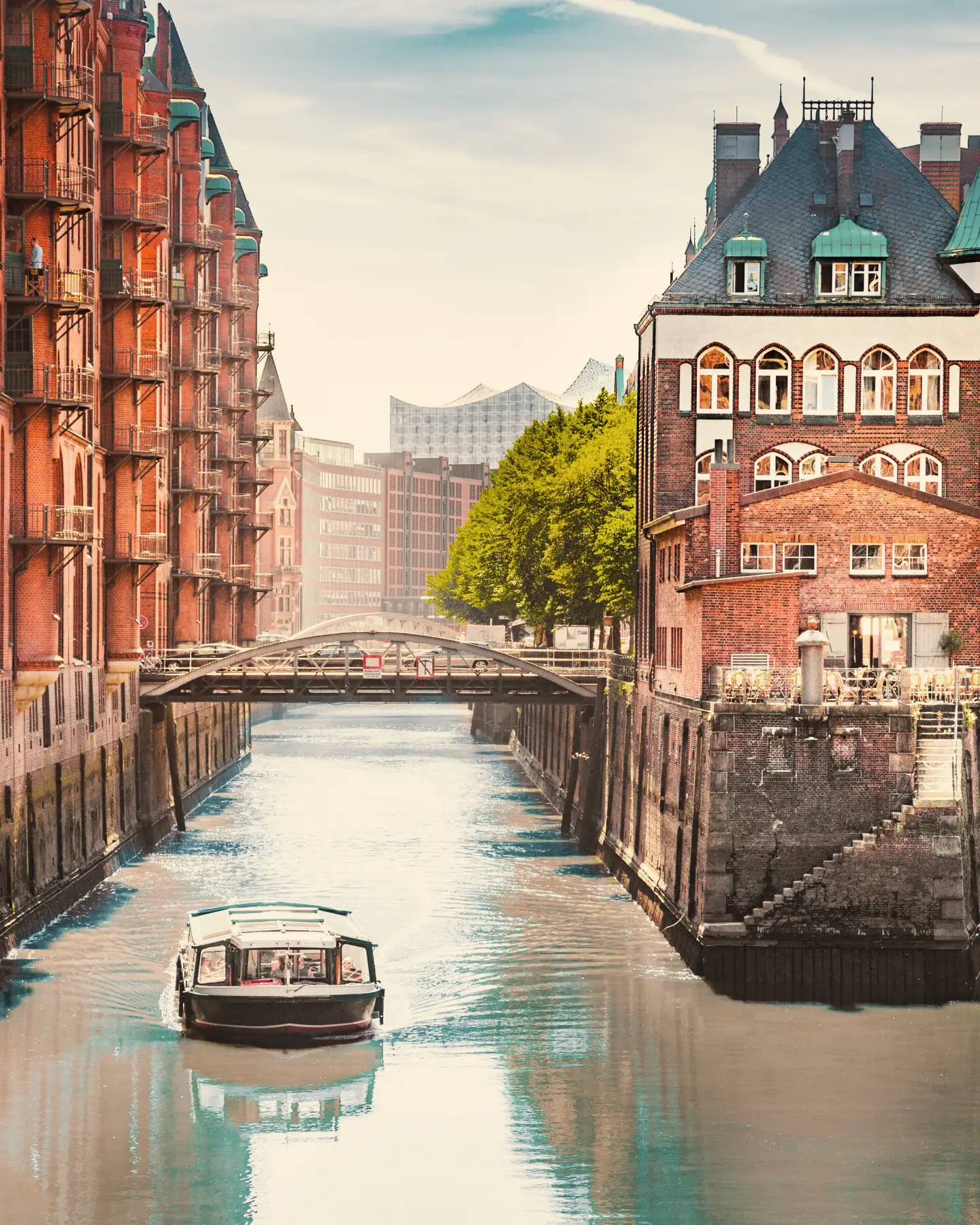 Wasserschloss in der Hamburger Speicherstadt mit Backsteinfassaden, Kanälen, Brücken und einem Ausflugsboot auf dem Wasser bei weichem Tageslicht