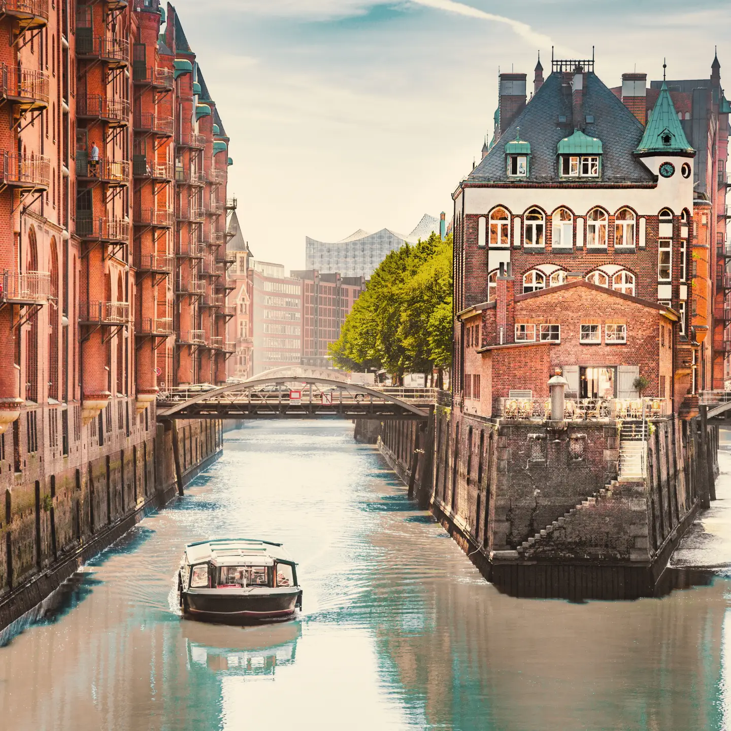 Wasserschloss in der Hamburger Speicherstadt mit Backsteinfassaden, Kanälen, Brücken und einem Ausflugsboot auf dem Wasser bei weichem Tageslicht