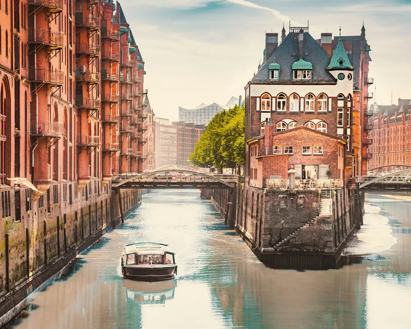 La Speicherstadt de Hamburgo con edificios históricos de ladrillo rojo, un canal de agua, un puente y un barco navegando por las aguas tranquilas.