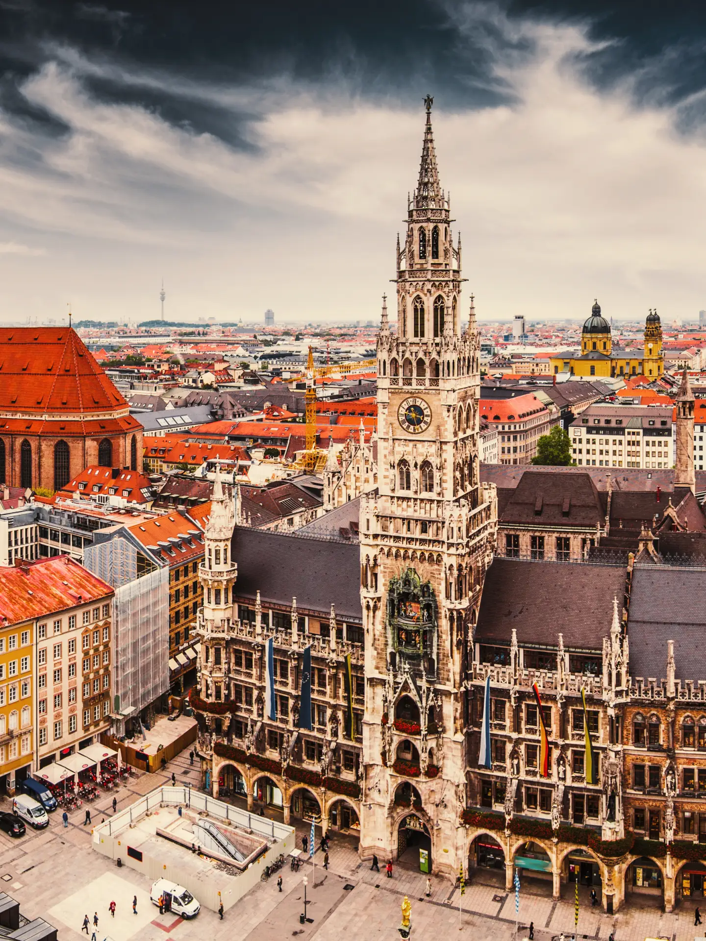 Panoramic view of the old town of Munich, Germany, with the New Town Hall and the Frauenkirche in the foreground under a dramatic sky.