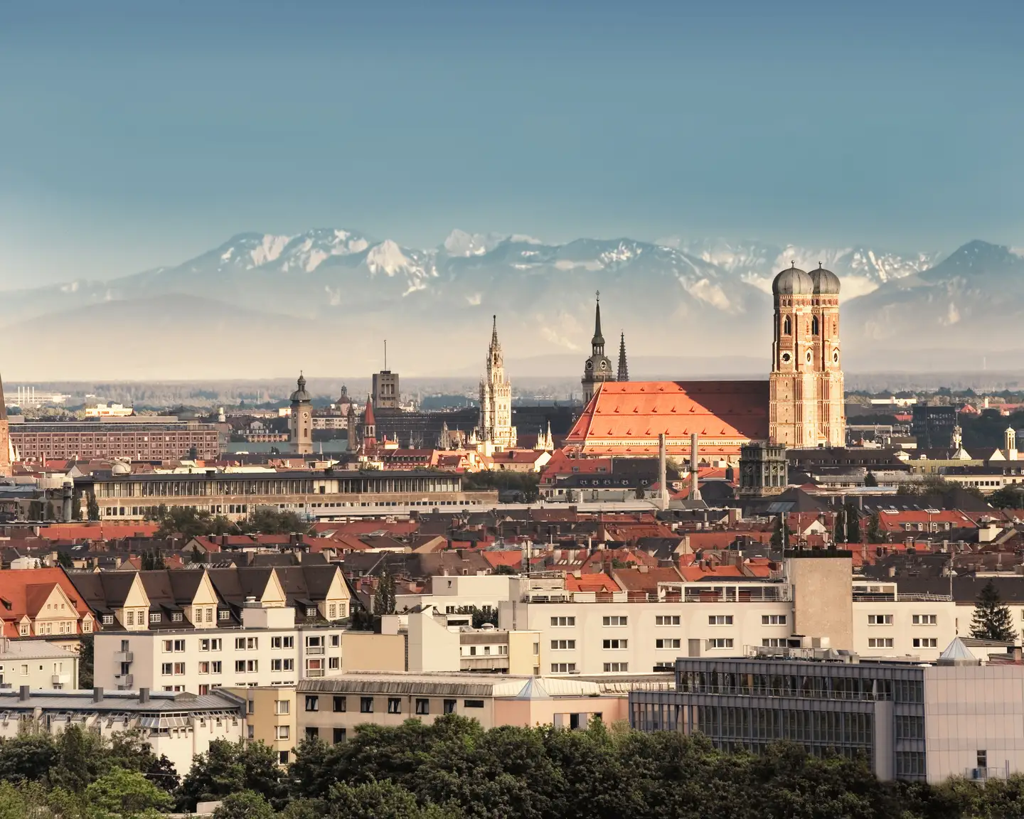 Panorama de Múnich con la Frauenkirche y otros edificios históricos del centro de la ciudad, con los Alpes al fondo bajo un cielo despejado.