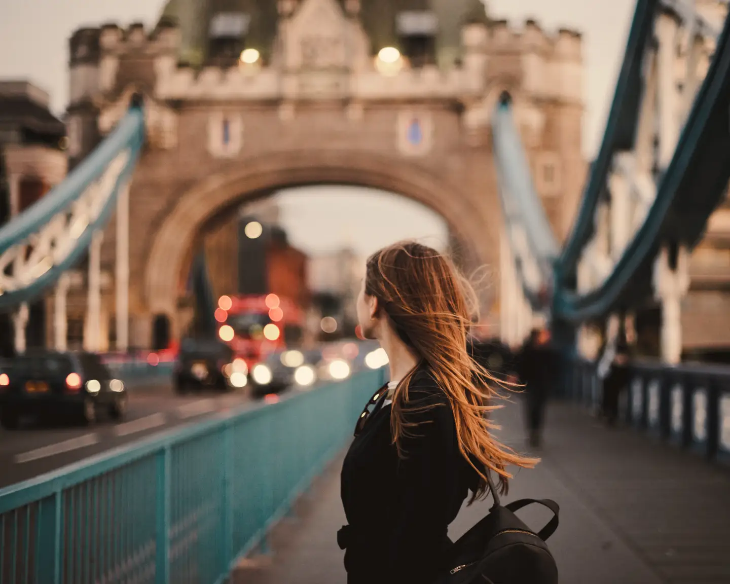 Frau mit langen Haaren steht vor der Tower Bridge in London.