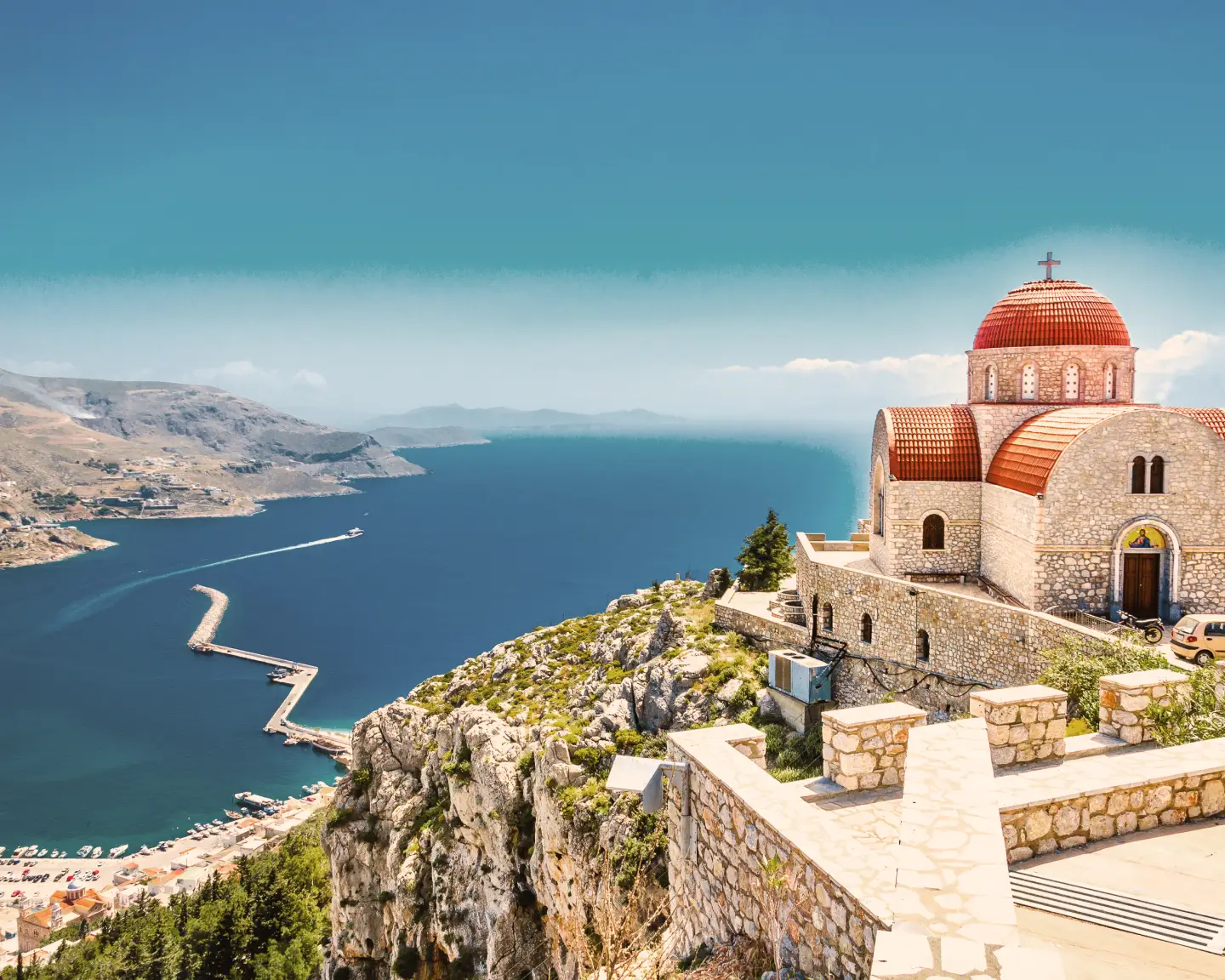 Vue panoramique du monastère Agios Savvas à Corfou, en Grèce, avec un dôme rouge, une vue sur la mer et un port.