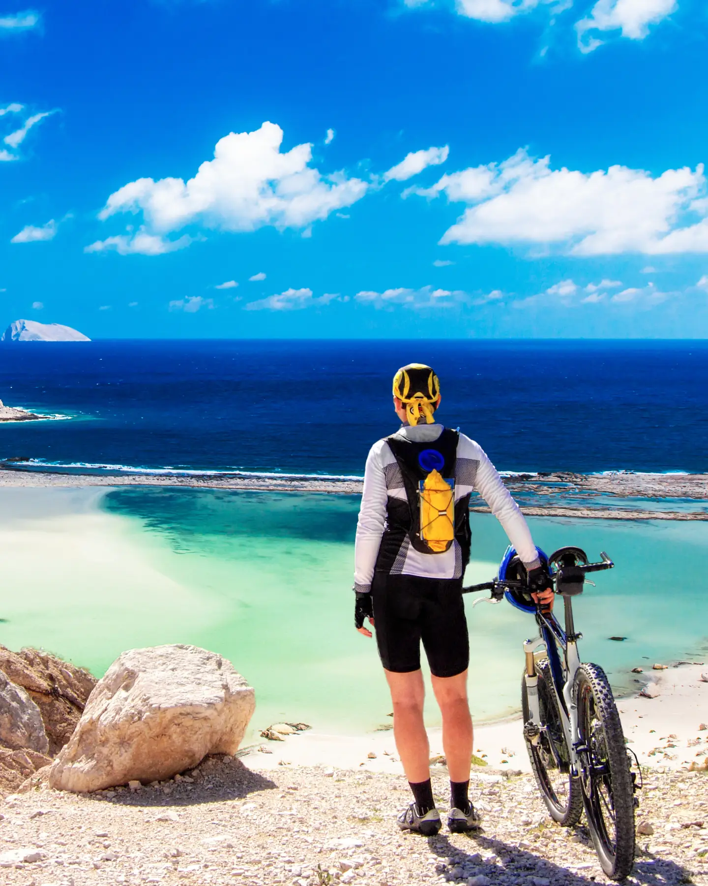 Ein Mountainbiker steht am Ufer der Balos Lagune auf Kreta, umgeben von kristallklarem Wasser und malerischen Felsenformationen.