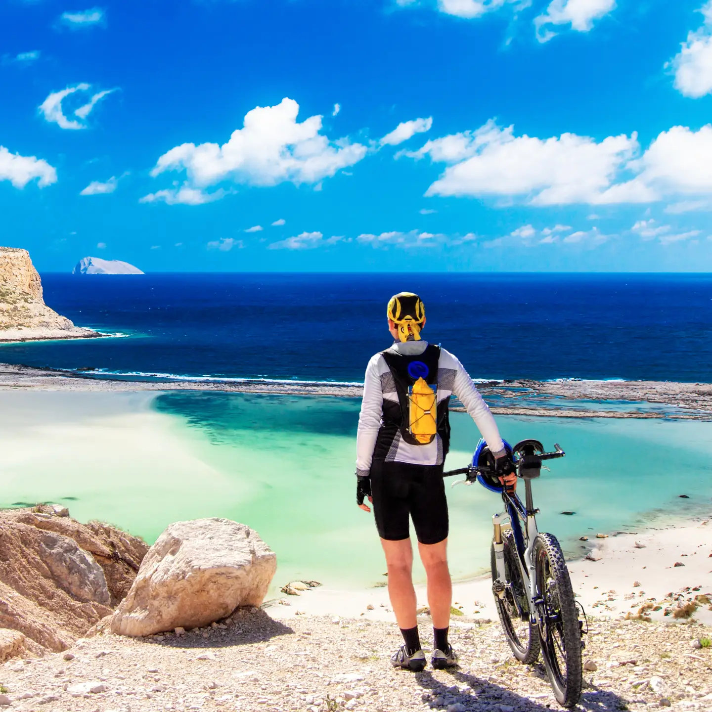 Ein Mountainbiker steht am Ufer der Balos Lagune auf Kreta, umgeben von kristallklarem Wasser und malerischen Felsenformationen.