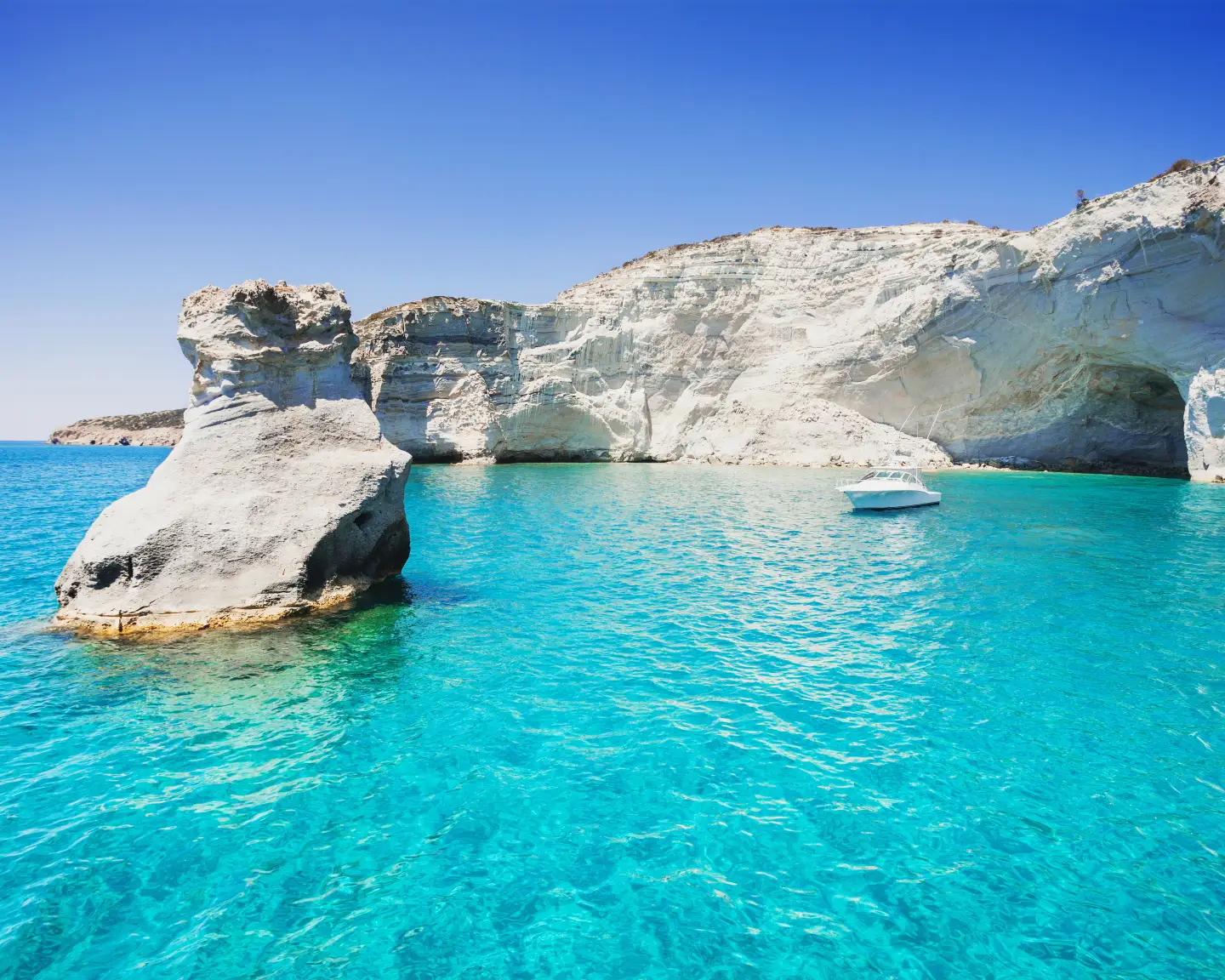 Türkisblaues Wasser, weiße Felsformationen und ein Boot in der Bucht von Sarakiniko auf der griechischen Insel Milos.