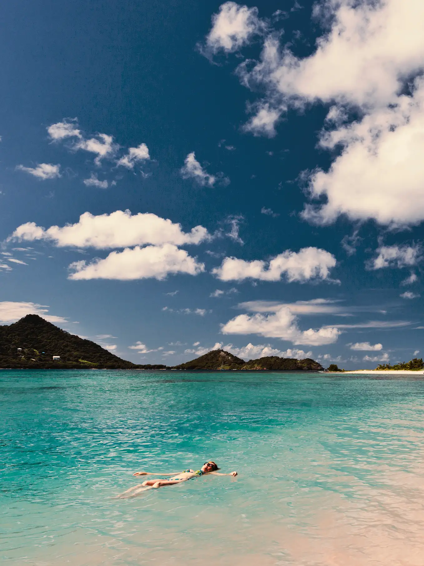 Mujer bañándose en el mar en la isla caribeña de Granada, con montañas boscosas al fondo.
