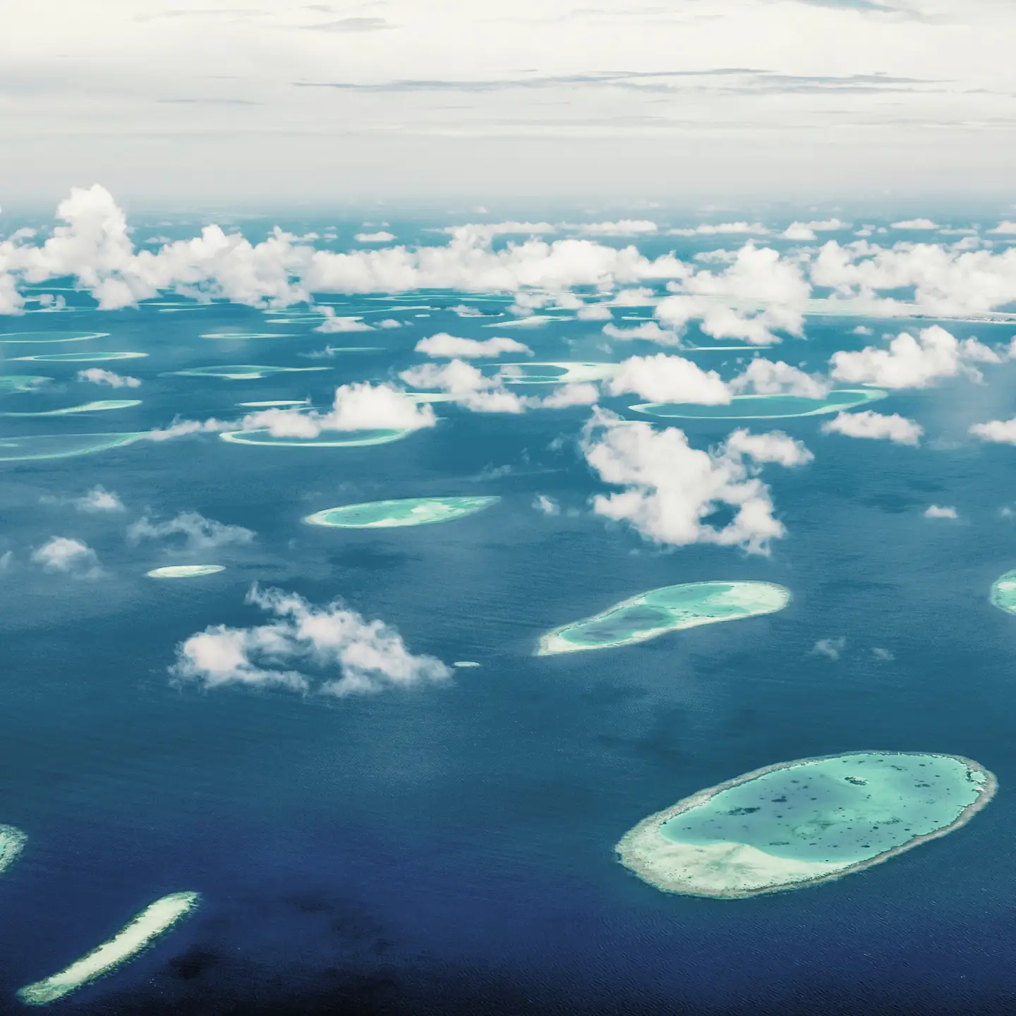 Vue aérienne des Maldives avec de nombreuses petites îles et atolls dans la mer turquoise, entourées de nuages blancs.