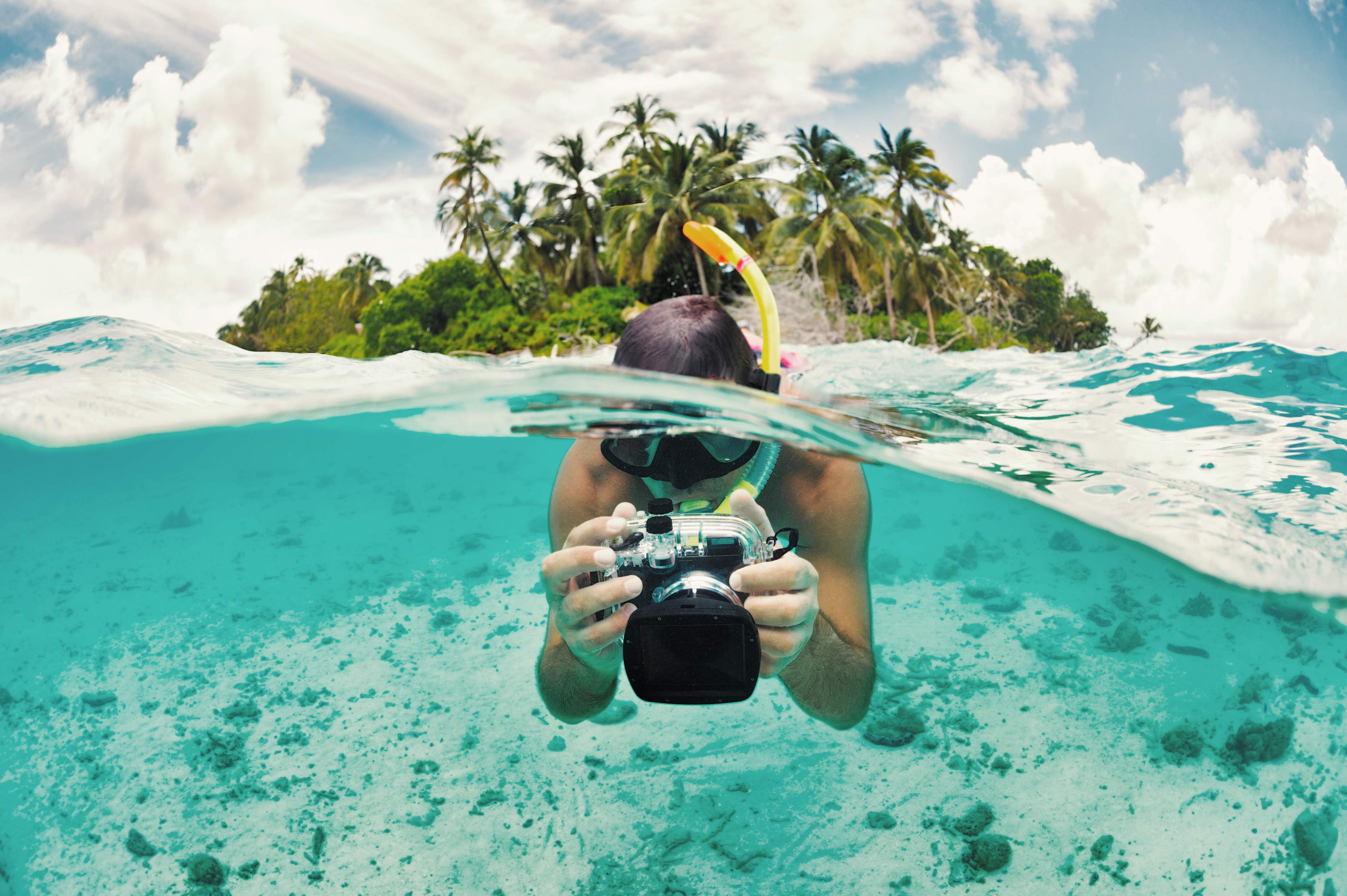 Un buceador con un snorkel y cámara subacuática hace fotos al ras del agua en una isla tropical. Un buceador con un snorkel y cámara subacuática hace fotos al ras del agua en una isla tropical.