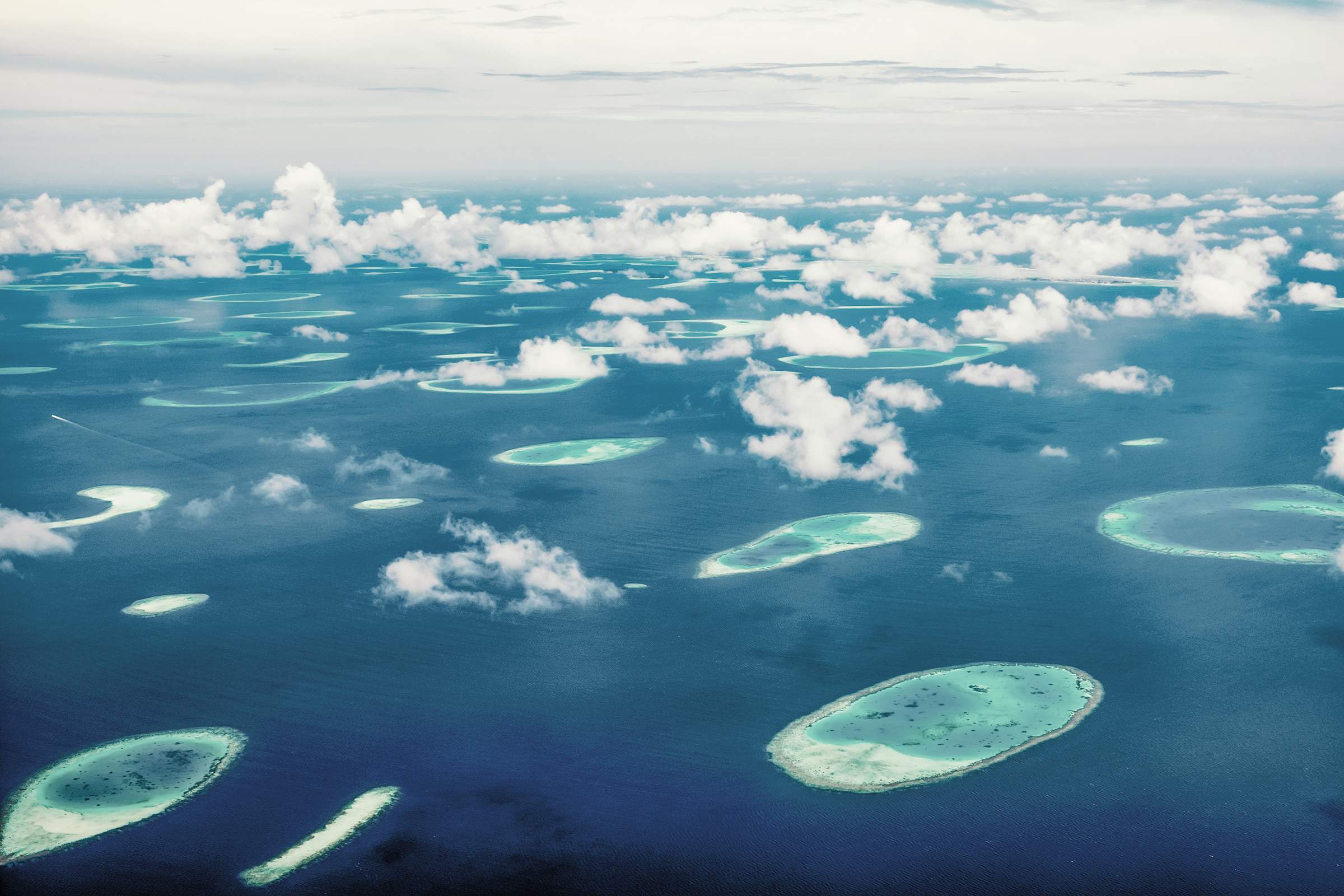Vista aérea de las Maldivas con numerosas islas pequeñas y atolones en el mar turquesa, rodeadas de nubes blancas.