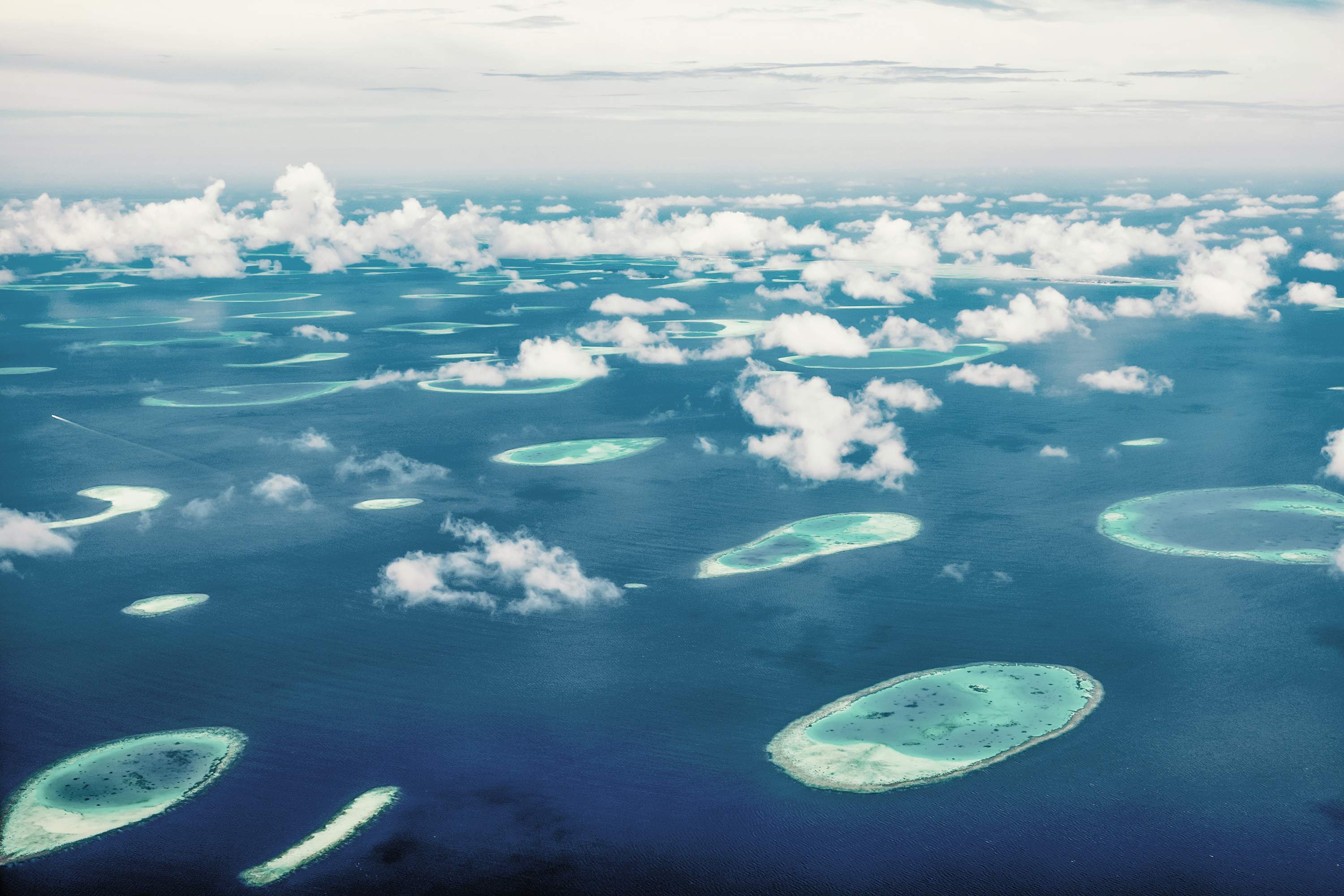 Luchtfoto van de Malediven met talrijke kleine eilanden en atollen in de turquoise zee, omgeven door witte wolken.