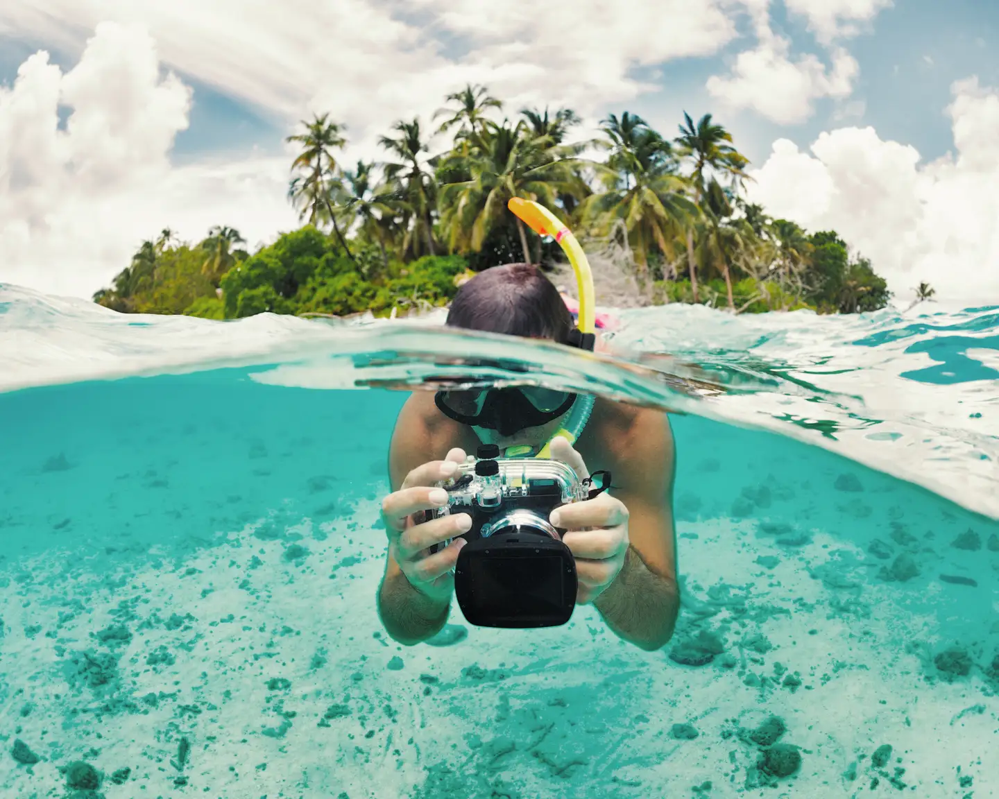 Un submarinista con tubo de bucear y cámara subacuática hace fotos a ras del agua en una isla tropical. Un submarinista con tubo de bucear y cámara subacuática hace fotos a ras del agua en una isla tropical.