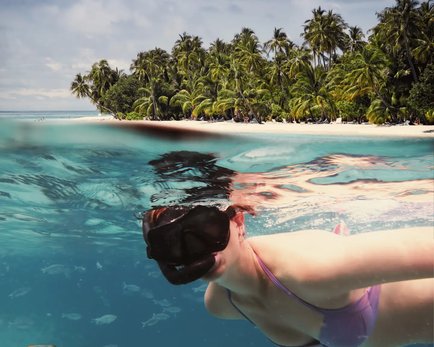 Über- und Unterwasseraufnahme einer Frau beim Schnorcheln vor einer tropischen Insel
