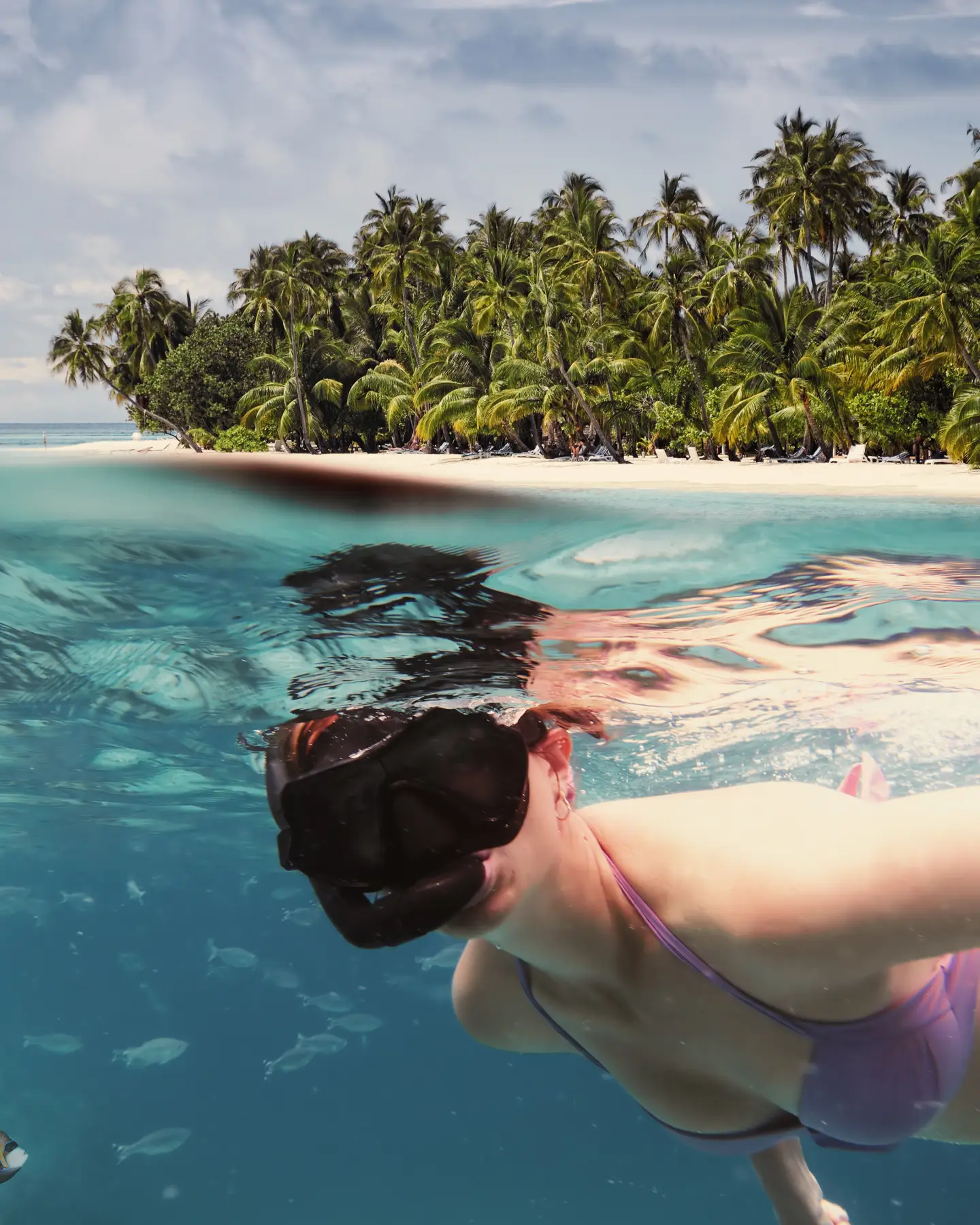 Une femme fait du snorkeling dans les eaux cristallines et turquoises d'une plage tropicale de l'île Maurice, entourée de palmiers.