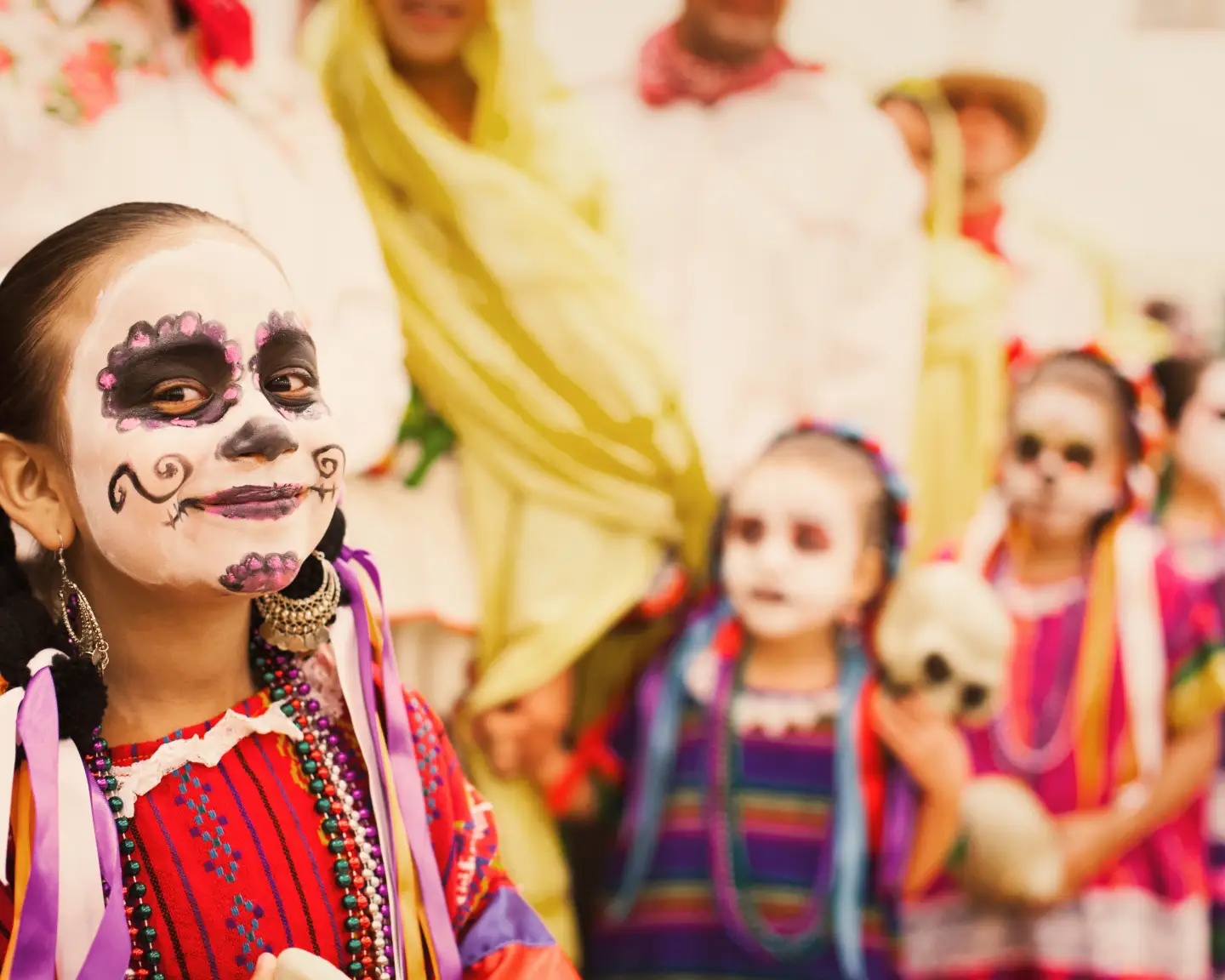 Ein lächelndes Mädchen mit wunderschönem traditionellem Make-up und einem farbenfrohen traditionellen Kleid zum Día de los Muertos in Mexiko.