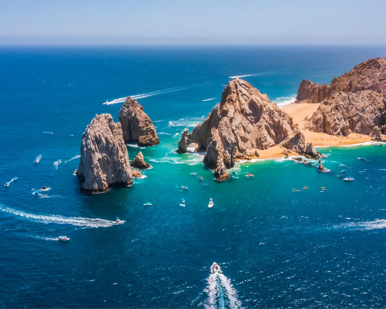 Aerial view of Cabo San Lucas, with impressive rock formations in the turquoise blue sea and boats crossing the water.