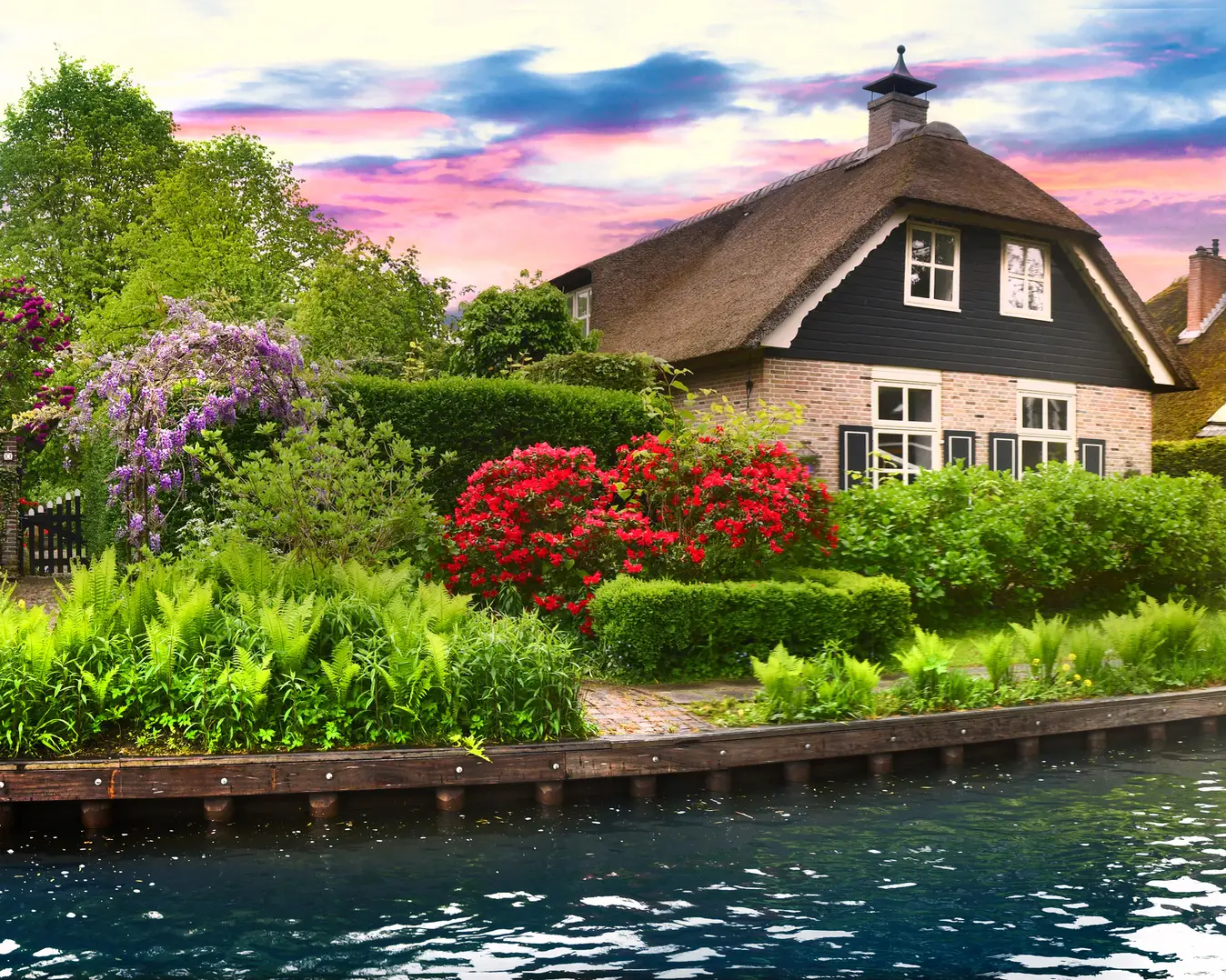 Landschaft des Dorfes Giethoorn mit Wasserkanälen und rustikalen Häusern in den Niederlanden – als Banner oder Panorama. Altes, kleines Backsteinhaus mit Reetdach und Holzbrücke.