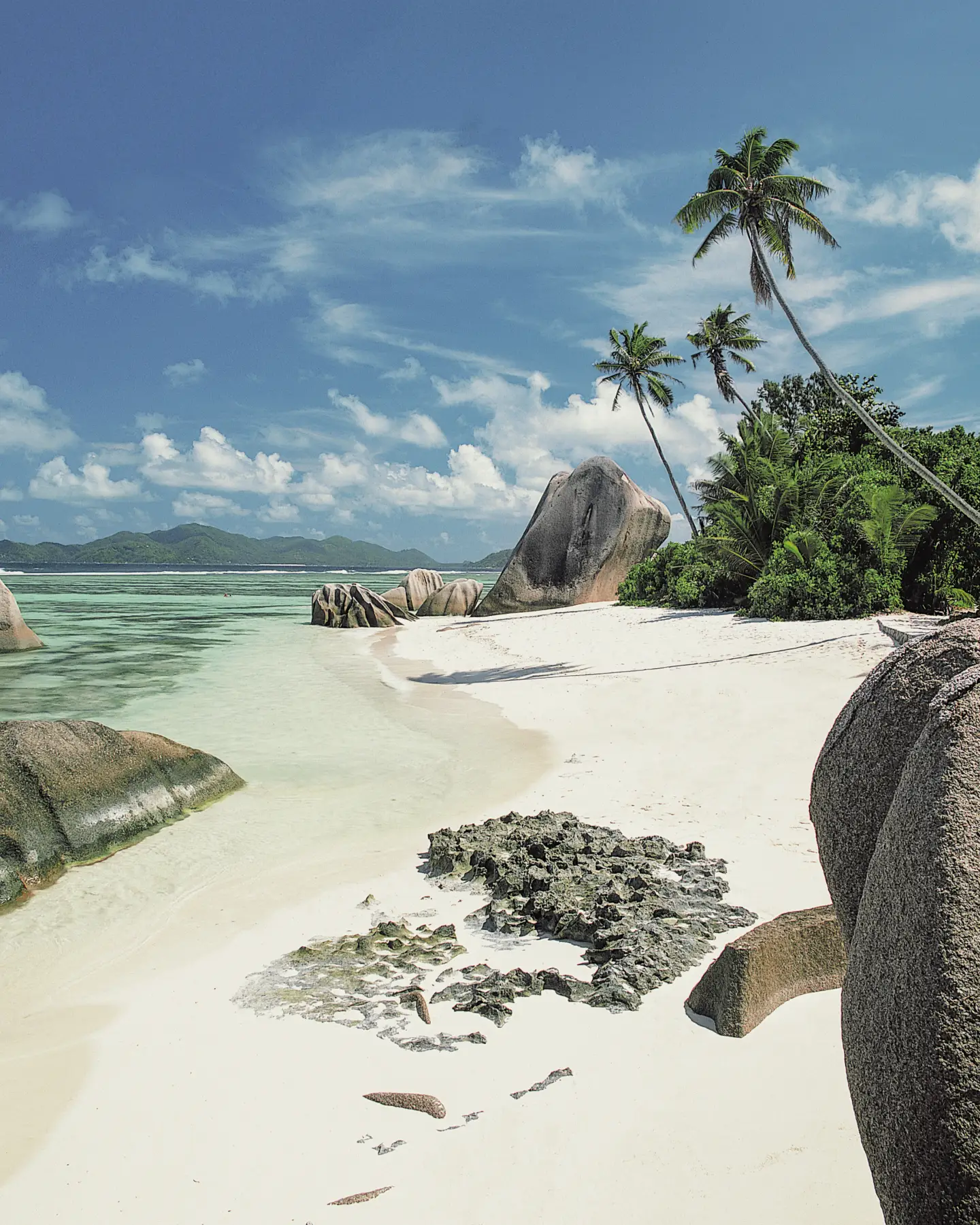 Az Anse Source d'Argent strand La Digue szigetén, a Seychelle-szigeteken, fehér homokkal, hatalmas gránitsziklákkal, pálmafákkal és tiszta, türkizkék vízzel a kék ég alatt.