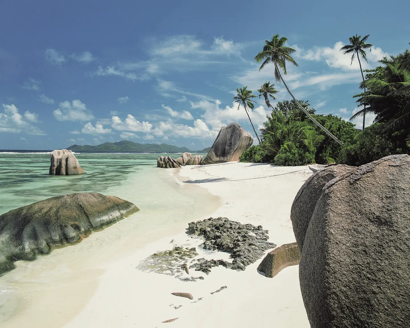 La playa de Anse Source d'Argent en La Digue, Seychelles, con arena blanca, grandes rocas de granito, palmeras y aguas cristalinas de color turquesa bajo el cielo azul.