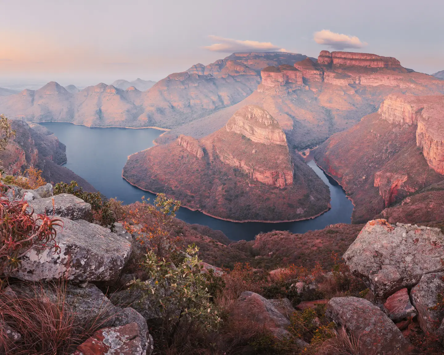 El cañón del río Blyde en las montañas Drakensberg de Sudáfrica, con impresionantes acantilados y un río rodeado de exuberante vegetación bajo la suave luz del atardecer.