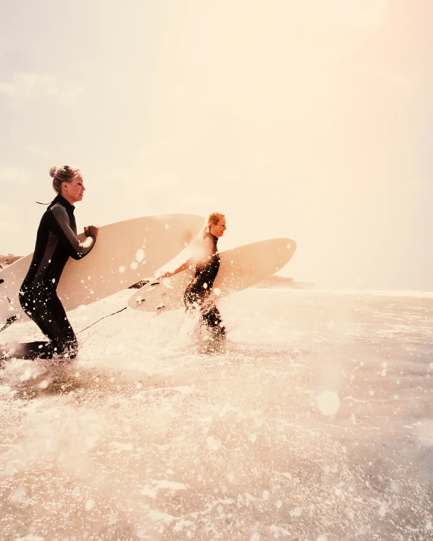 Two wetsuit-clad surfers plunging into the crashing sea off Fuerteventura with their surfboards, ready to conquer the waves.