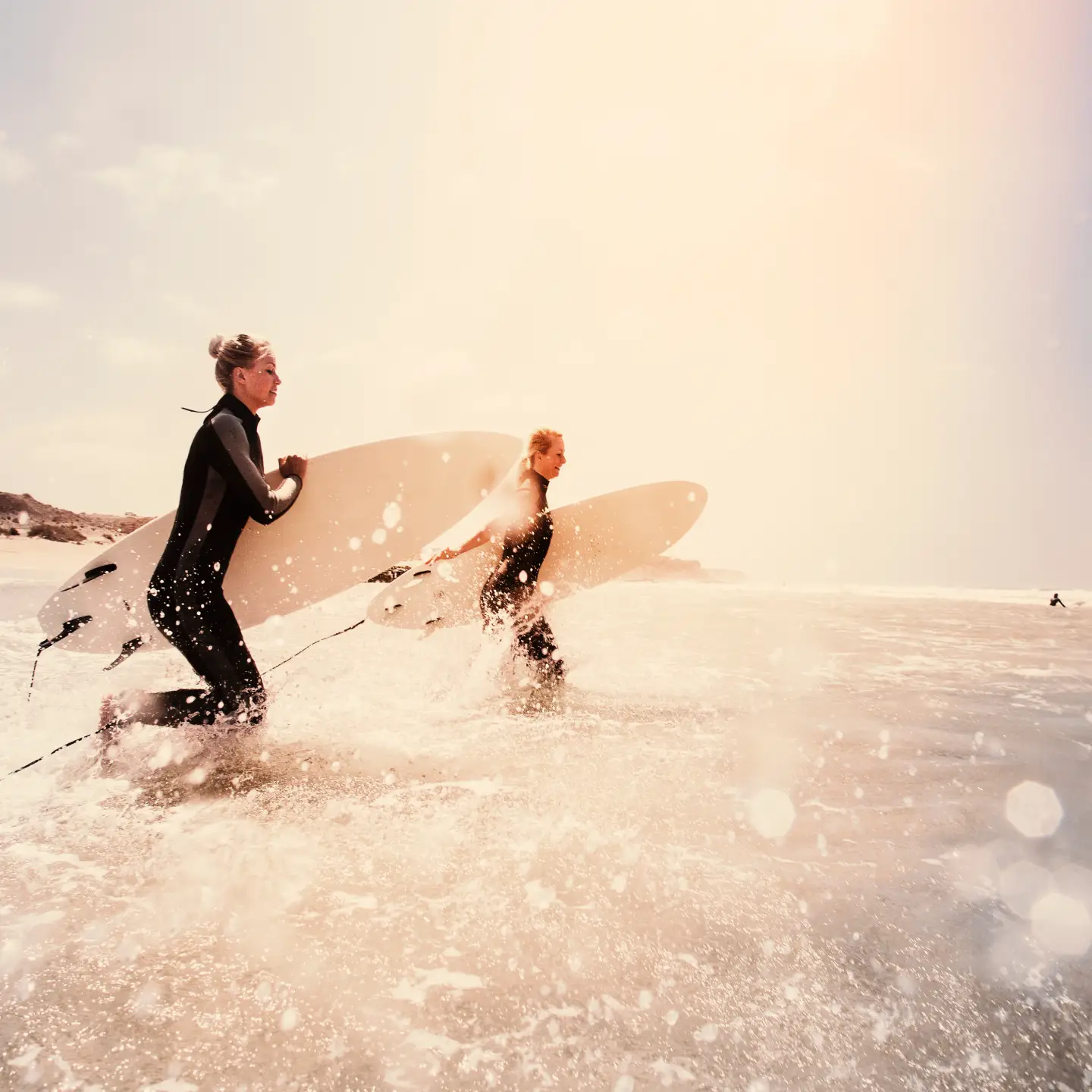 Two wetsuit-clad surfers plunging into the crashing sea off Fuerteventura with their surfboards, ready to conquer the waves.