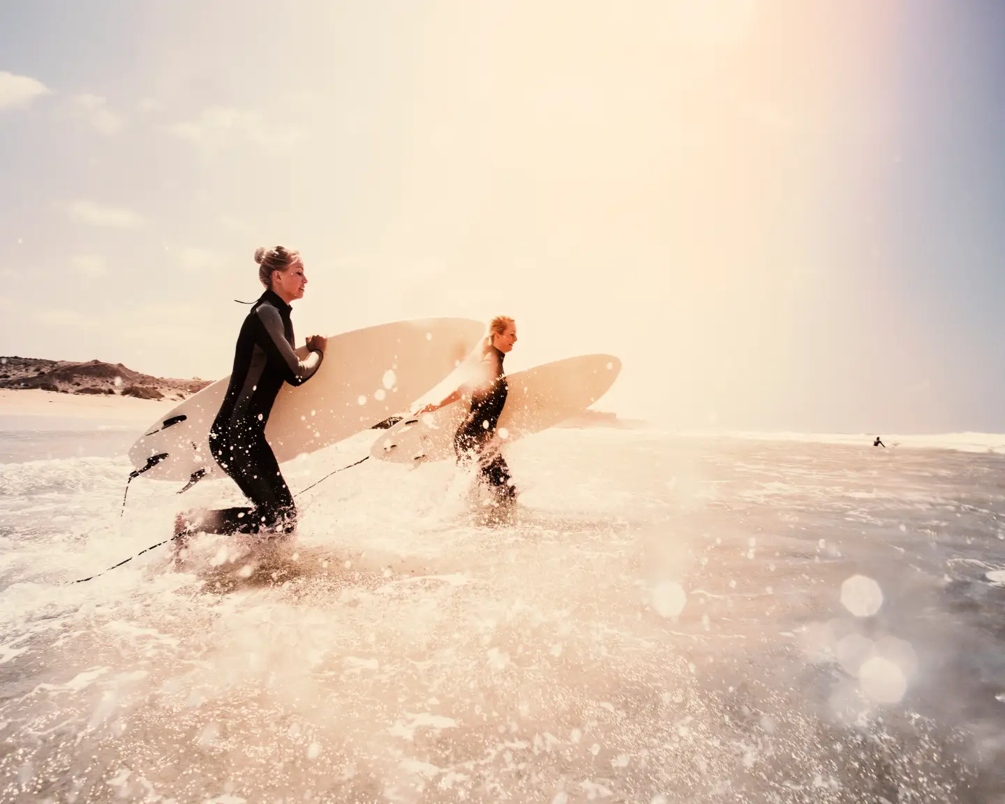 Zwei Surfer, ausgestattet mit Neoprenanzügen und Surfbrettern, stürzen sich ins spritzende Meerwasser von Fuerteventura, bereit die Wellen zu erobern.