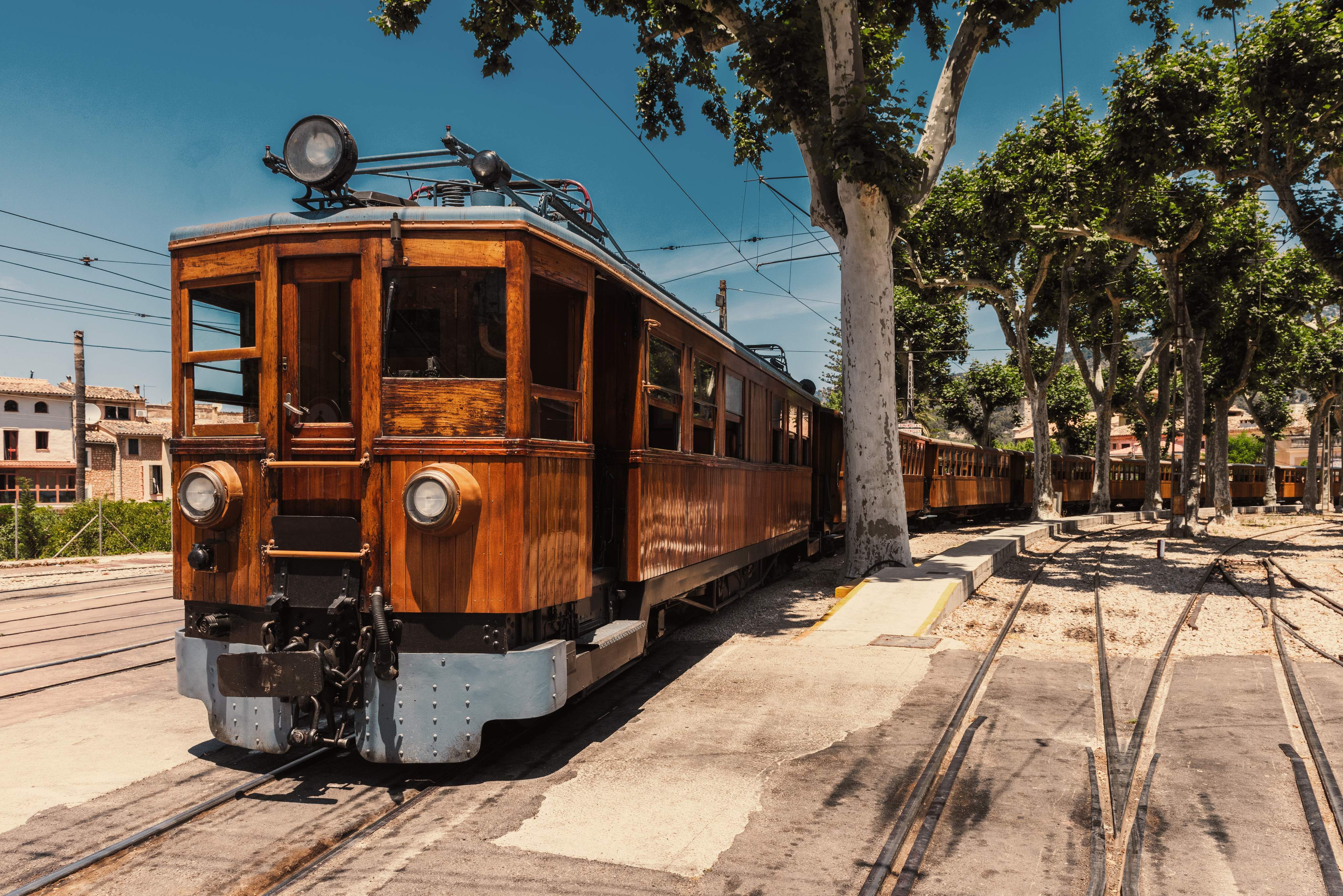 Historic streetcar on a sunny route, surrounded by trees.