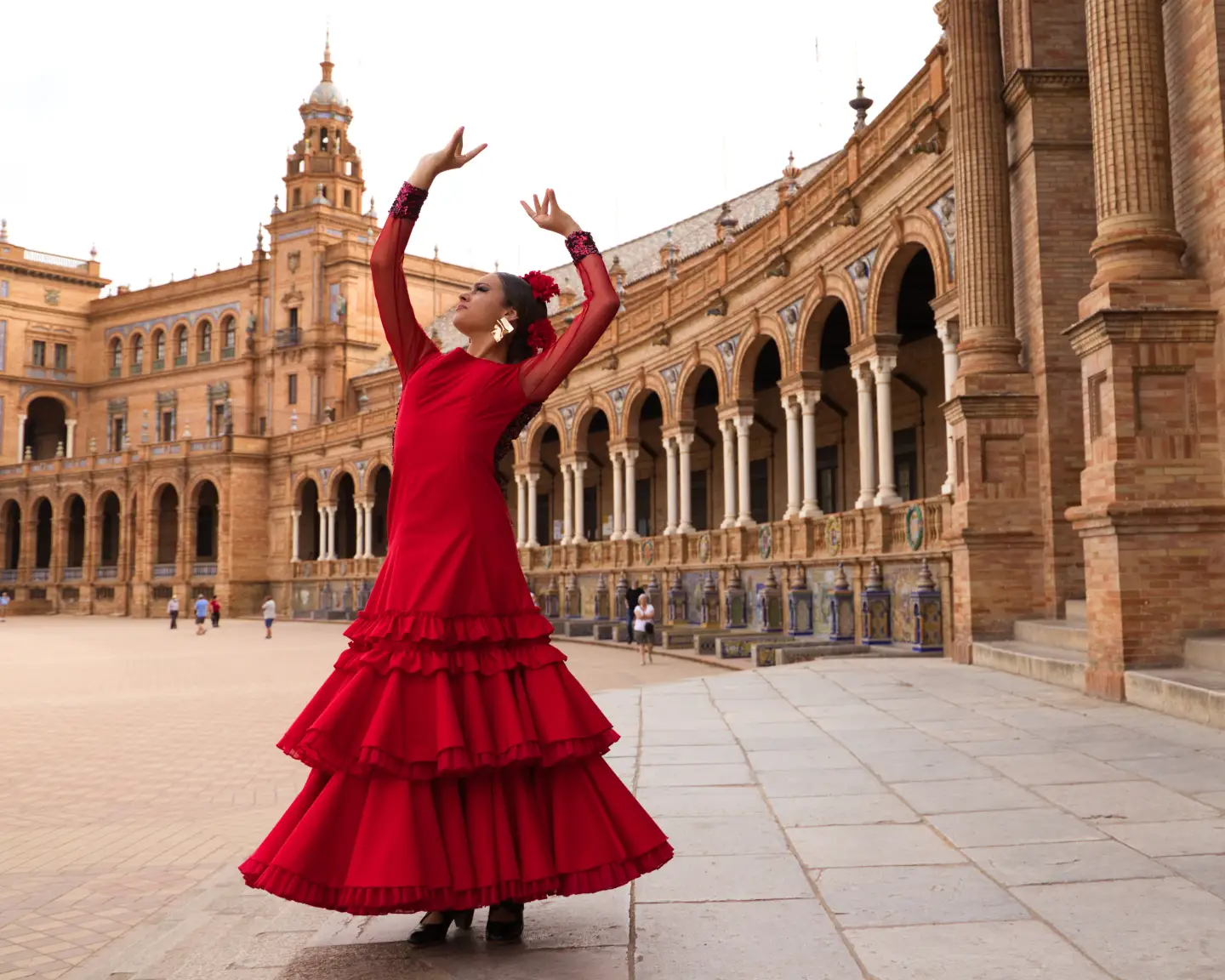 Eine schöne junge Frau tanzt Flamenco auf einem Platz in Sevilla, Spanien. Sie trägt ein rotes Kleid mit Rüschen und tanzt Flamenco mit viel künstlerischem Ausdruck. Flamenco – kulturelles Erbe der Menschheit.