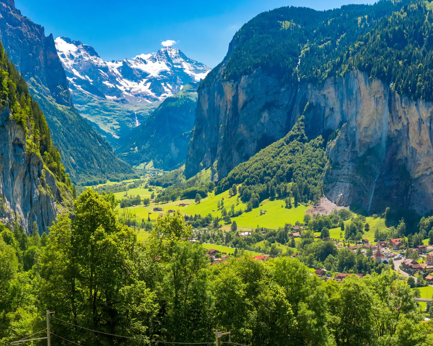 Panoramablick auf das Lauterbrunnental mit steilen Felswänden, grünen Wiesen und den schneebedeckten Gipfeln der Schweizer Alpen.