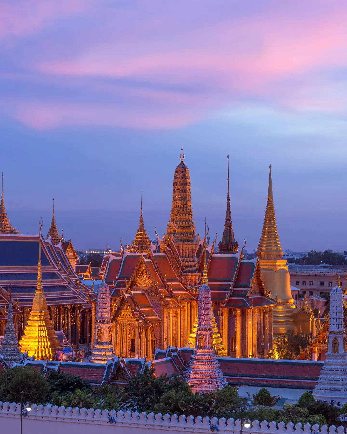 Vista nocturna del Gran Palacio iluminado en Bangkok, Tailandia, bajo un cielo vespertino lleno de color.