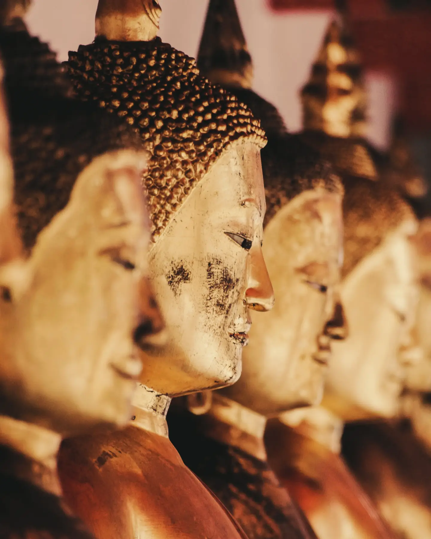 Közelkép arany Buddha szobrok soráról, amelyeket meleg fény világít meg a templom belsejében.