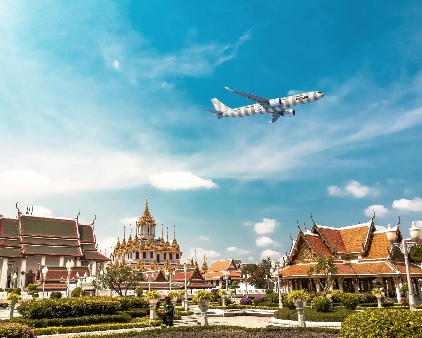 Een Condor-vliegtuig in zandkleur vliegt over een Thais tempelcomplex onder een blauwe hemel.