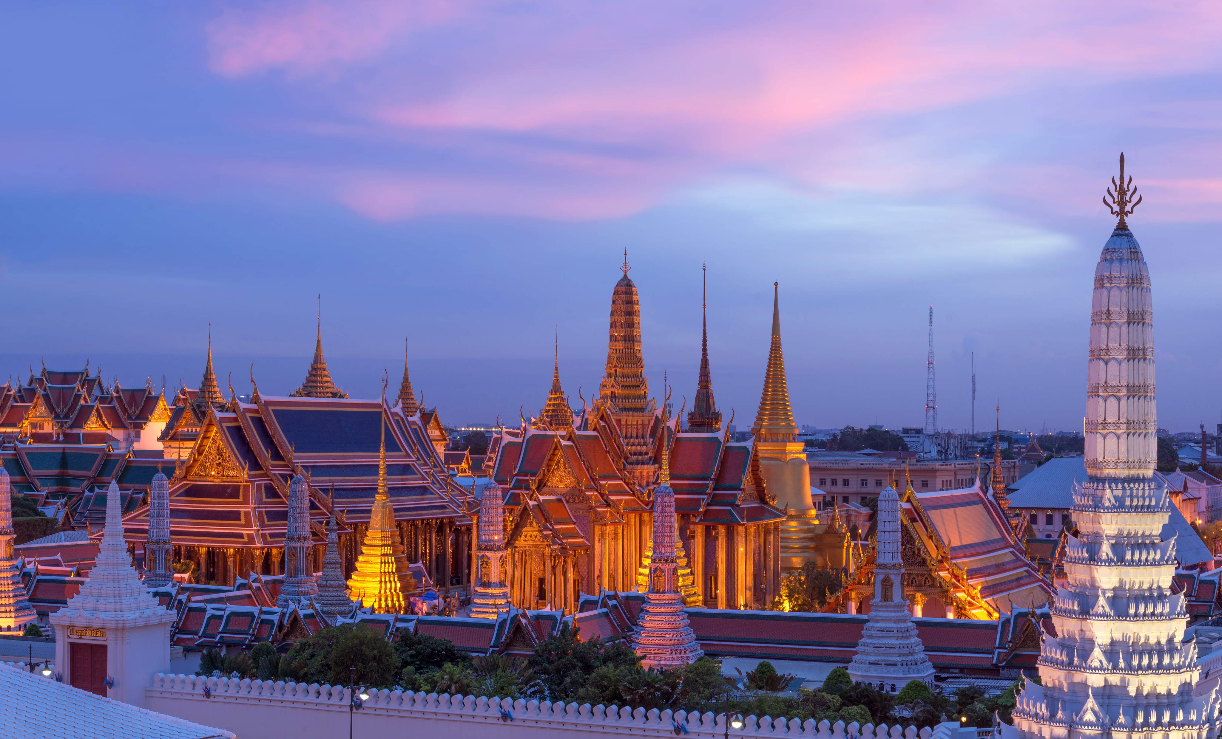Night view of the illuminated Grand Palace in Bangkok, Thailand, under a colourful evening sky.