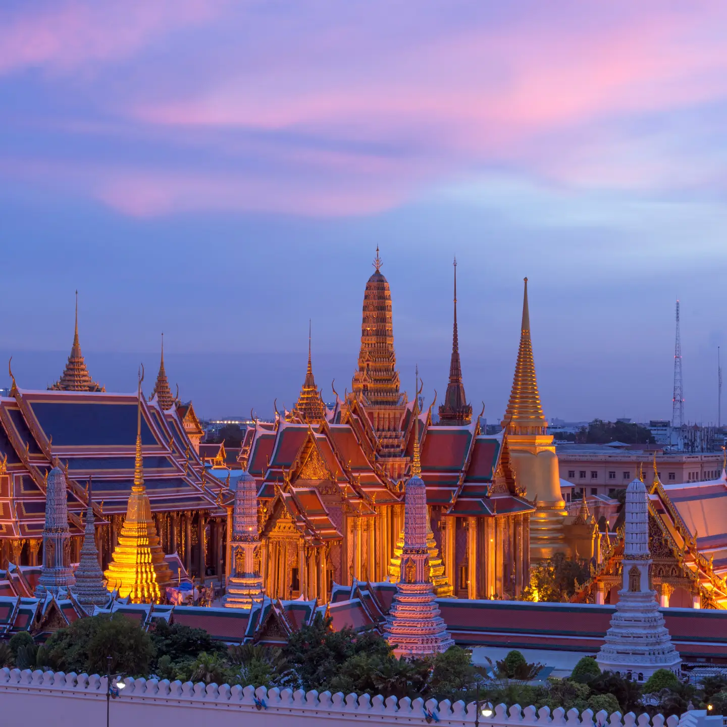 Night view of the illuminated Grand Palace in Bangkok, Thailand, under a colourful evening sky.