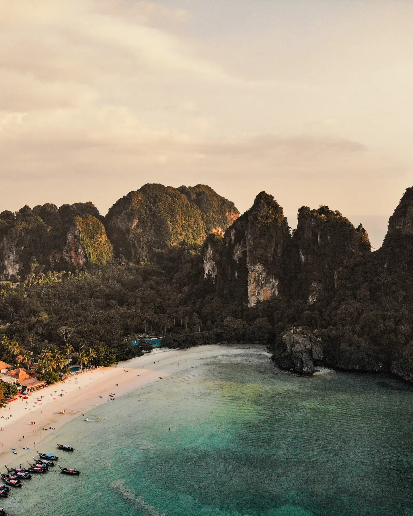 Aguas turquesas y una playa de arena blanca con un telón de fondo de exuberantes acantilados verdes en una bahía tropical.