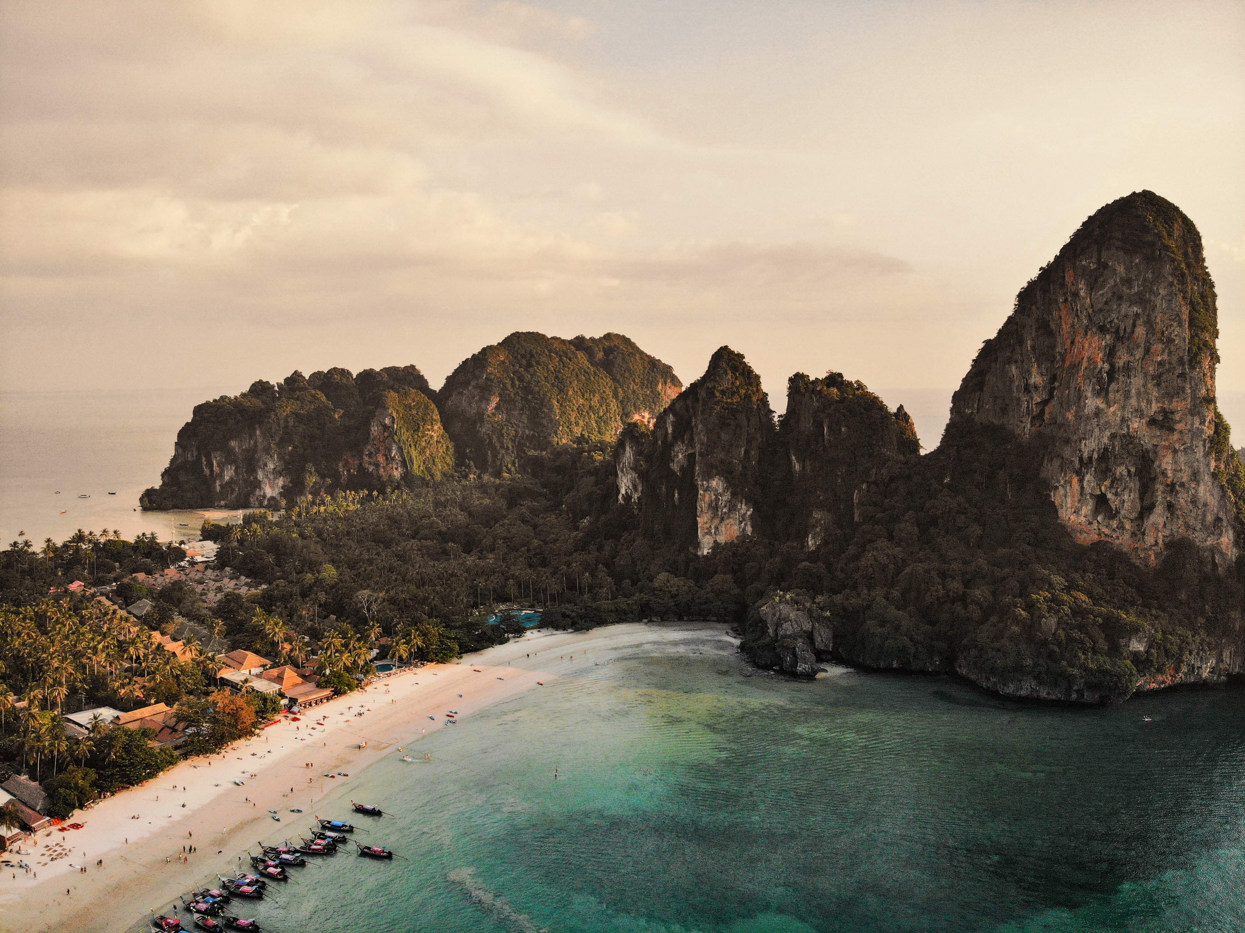Türkizkék vizek és fehér homokos strand buja zöld sziklák hátterében egy trópusi öbölben.
