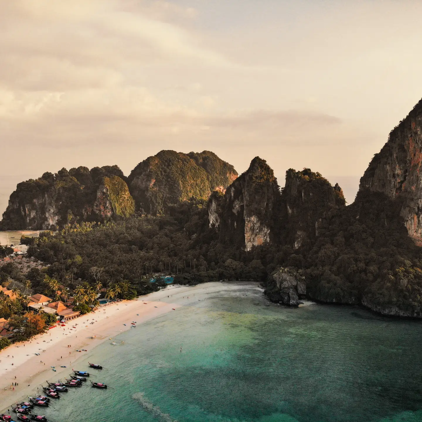 Turquoise wateren en een wit zandstrand tegen een achtergrond van weelderige groene kliffen in een tropische baai.