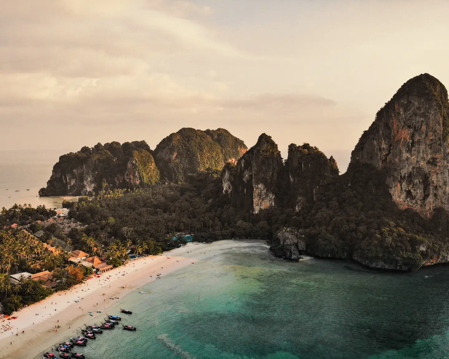 Eaux turquoise et plage de sable blanc sur fond de falaises verdoyantes dans une baie tropicale.