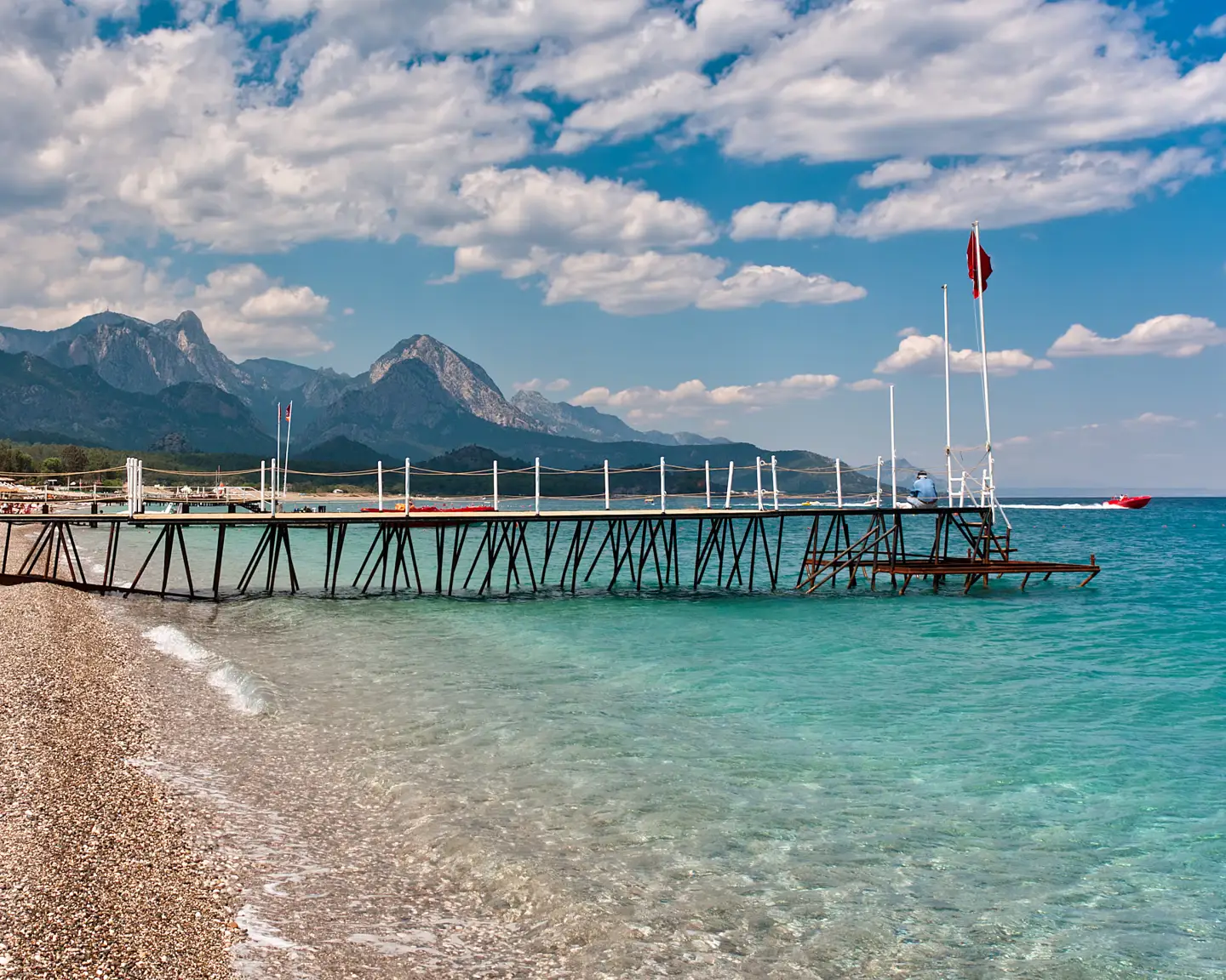 Small wooden jetty on a pebble beach with aquamarine water in the popular holiday resort of Kemer on the Mediterranean Sea in Turkey.