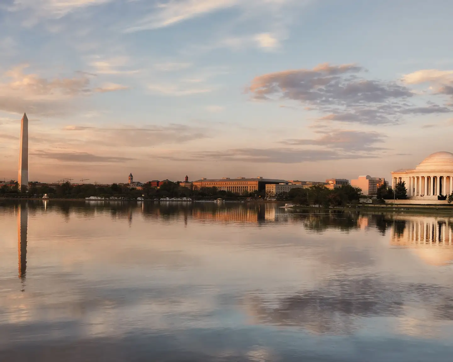 Pohled na Washingtonův monument a Jeffersonův památník při západu slunce, odrážející se ve vodě nádrže Tidal Basin ve Washingtonu, DC