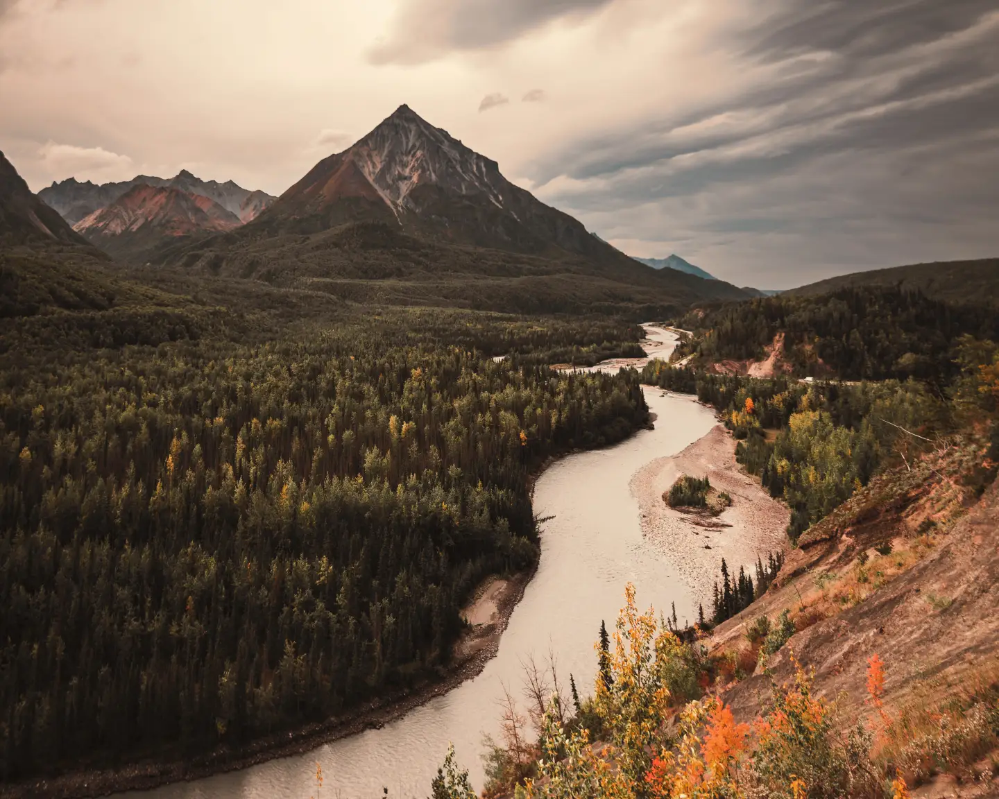 Un paysage fluvial pittoresque avec des collines boisées et une haute montagne en arrière-plan sous un spectaculaire ciel d'Alaska.